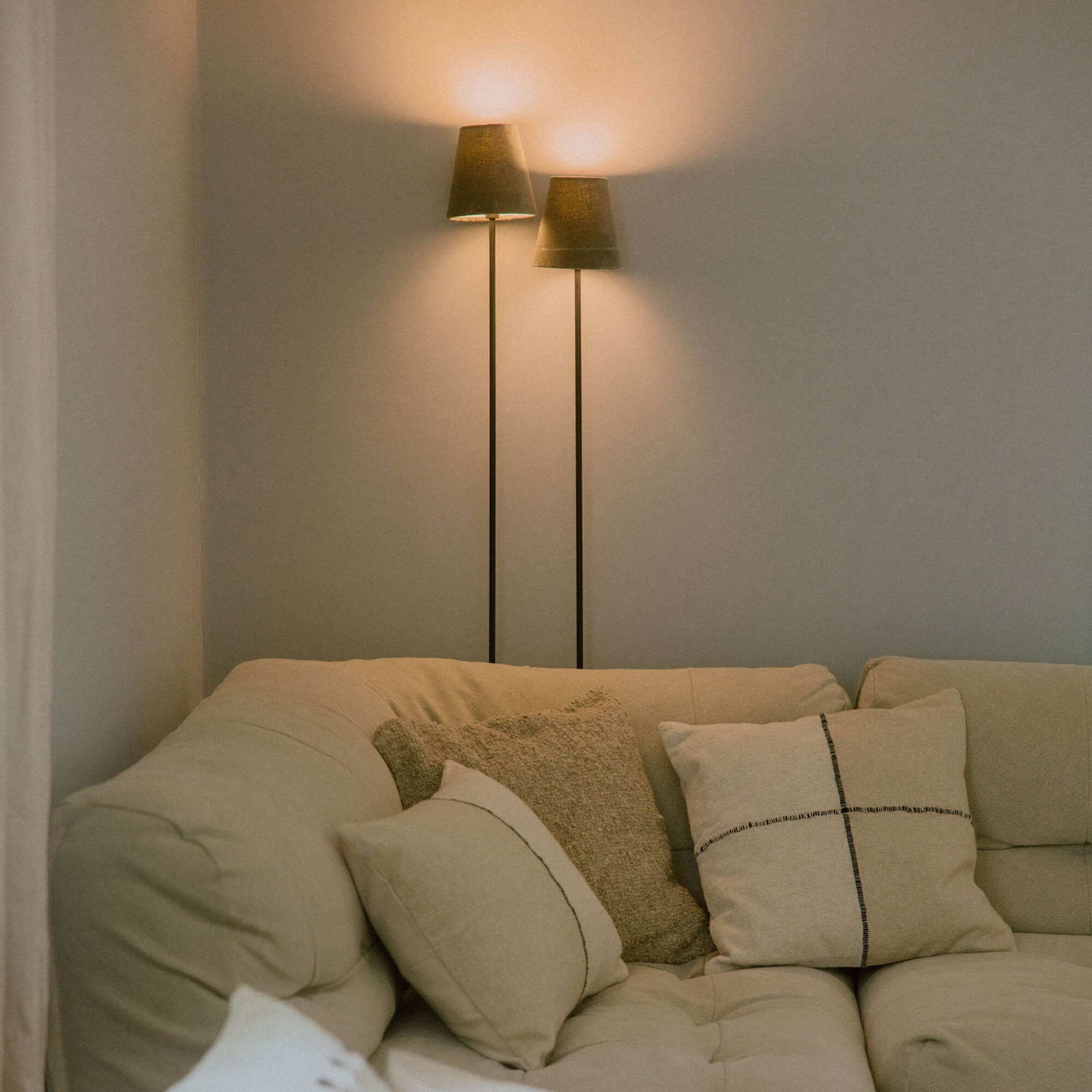 Canapé beige avec coussins doux et deux lampes sur pied à abat-jours foncés dans un salon