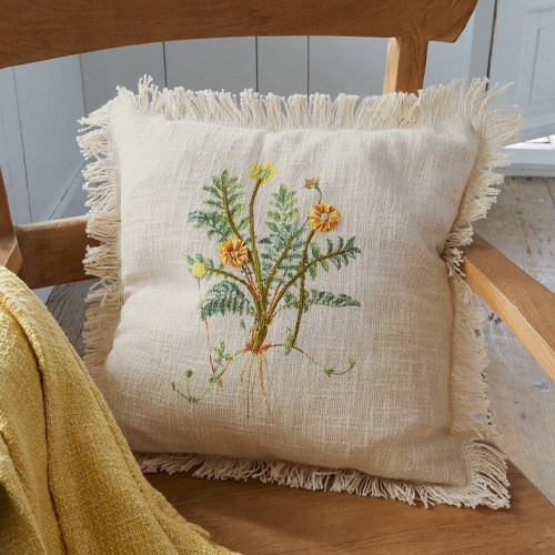 Coussin en lin beige avec franges et broderie florale sur chaise en bois clair