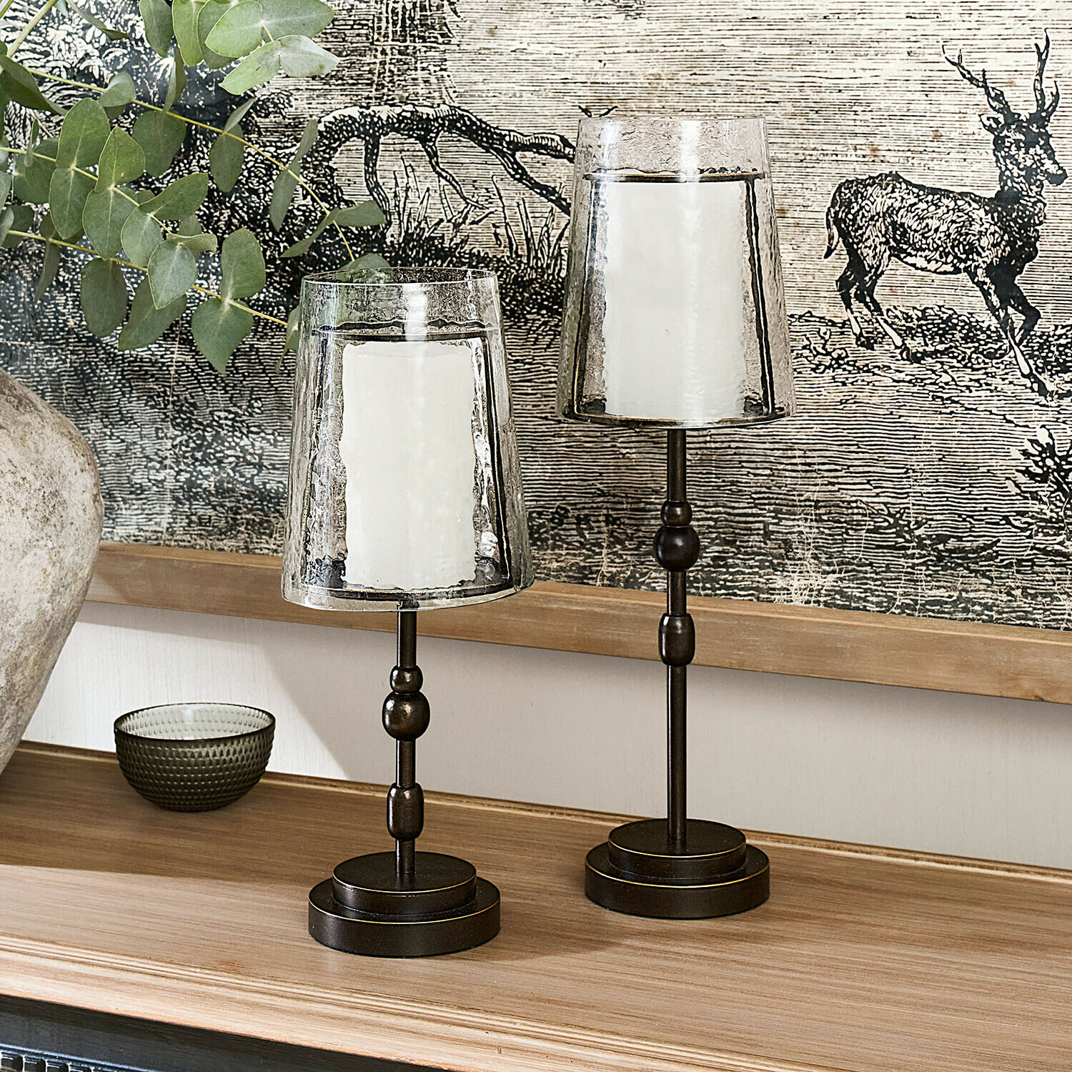 Deux bougeoirs en métal avec abat-jours en verre transparent et bougies blanches sur une surface en bois