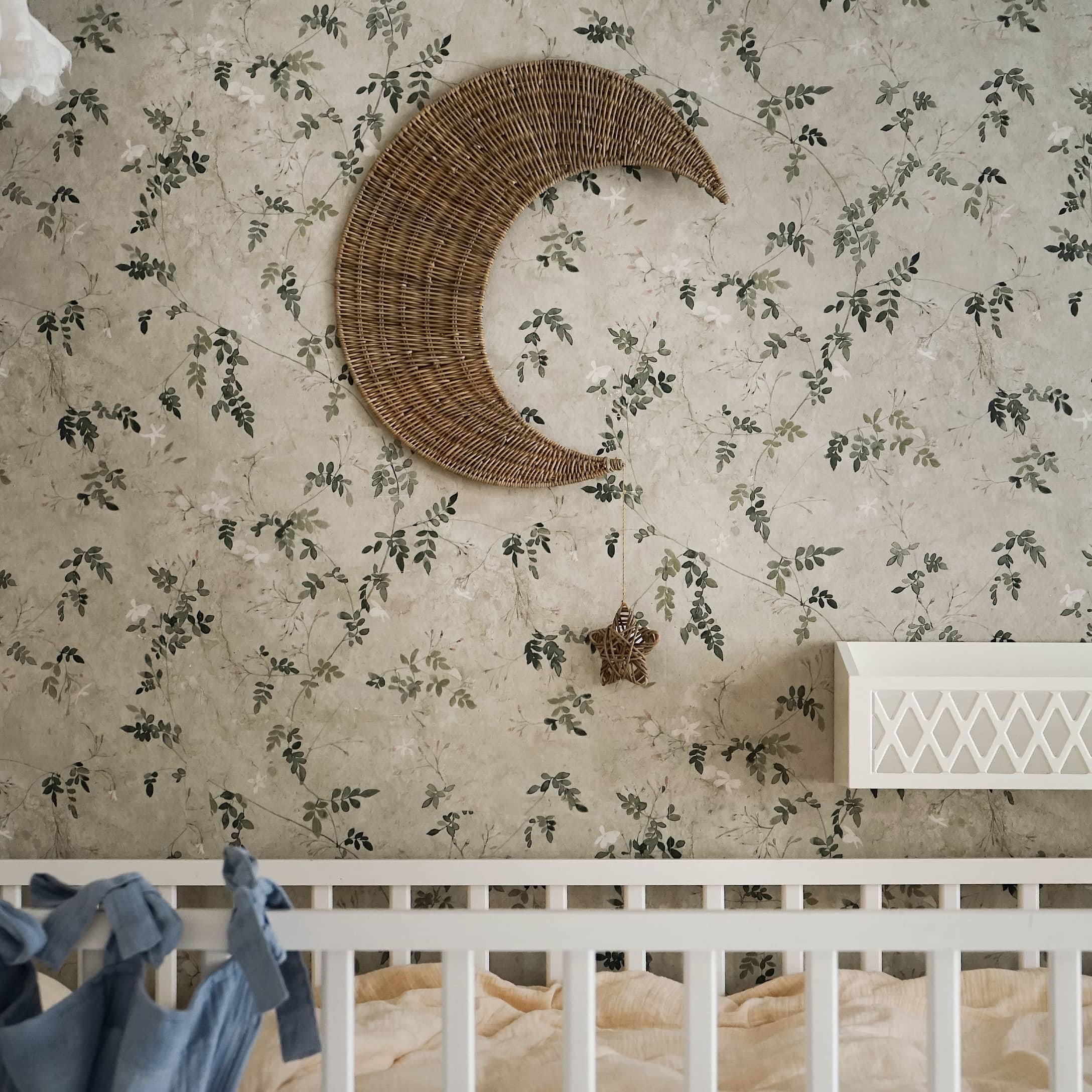 Décoration murale en osier en forme de lune avec une étoile suspendue sur un papier peint floral dans une chambre d'enfant