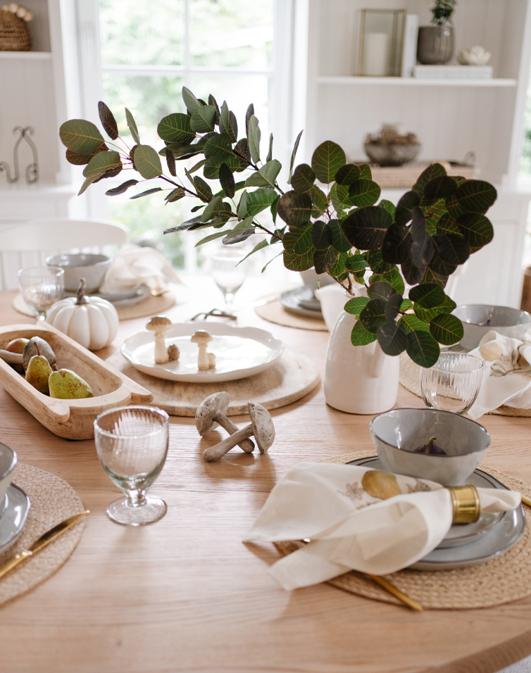 Table d'automne en bois clair avec décorations de feuilles, champignons et vaisselle élégante pour repas