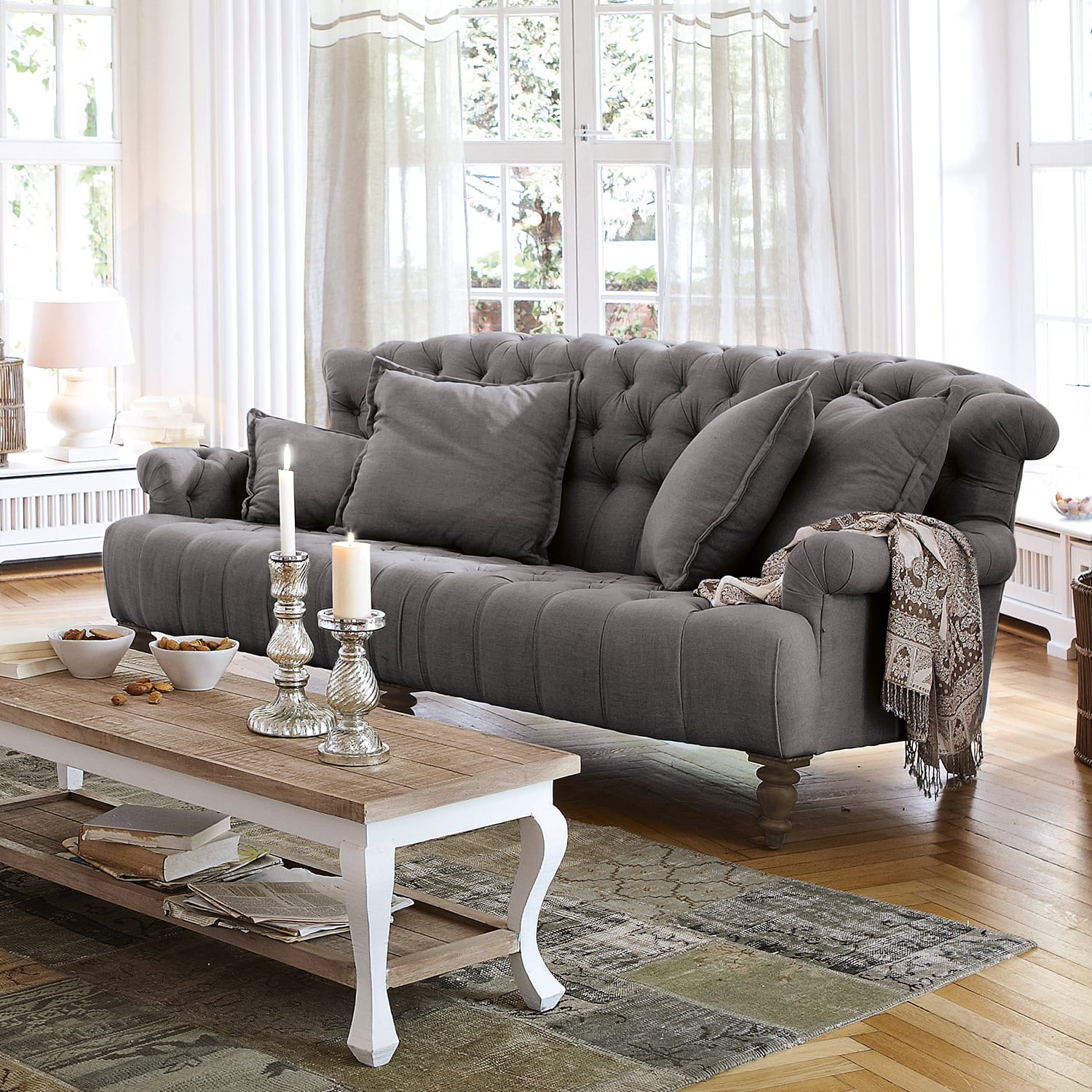 Canapé capitonné gris en tissu avec coussins et plaid décoratif dans un salon lumineux au sol en bois