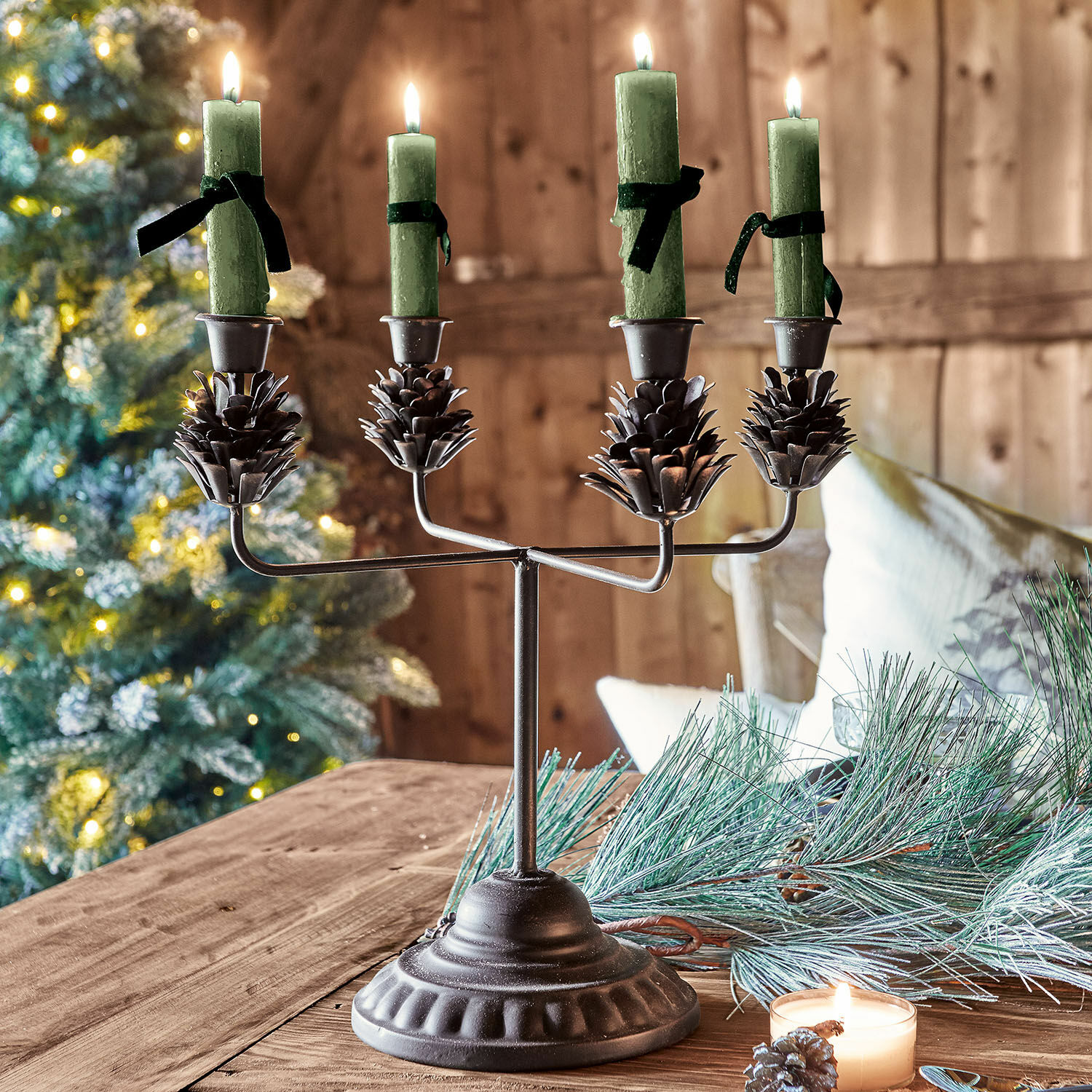 Bougeoir Spencer Chandelier en métal avec quatre bougies vertes et décorations pommes de pin sur table en bois