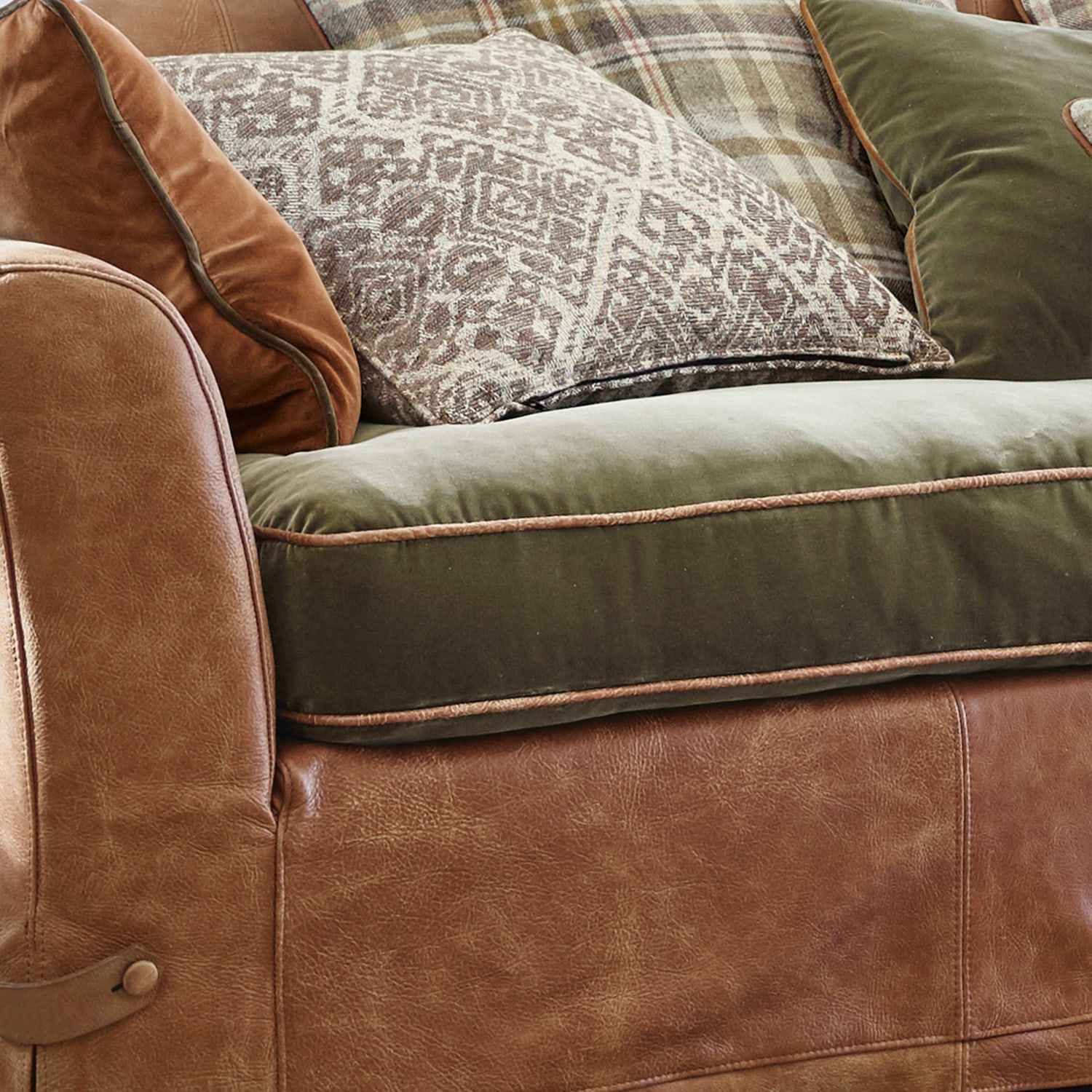Canapé en cuir marron avec assise en velours vert et coussins décoratifs à motifs rustiques