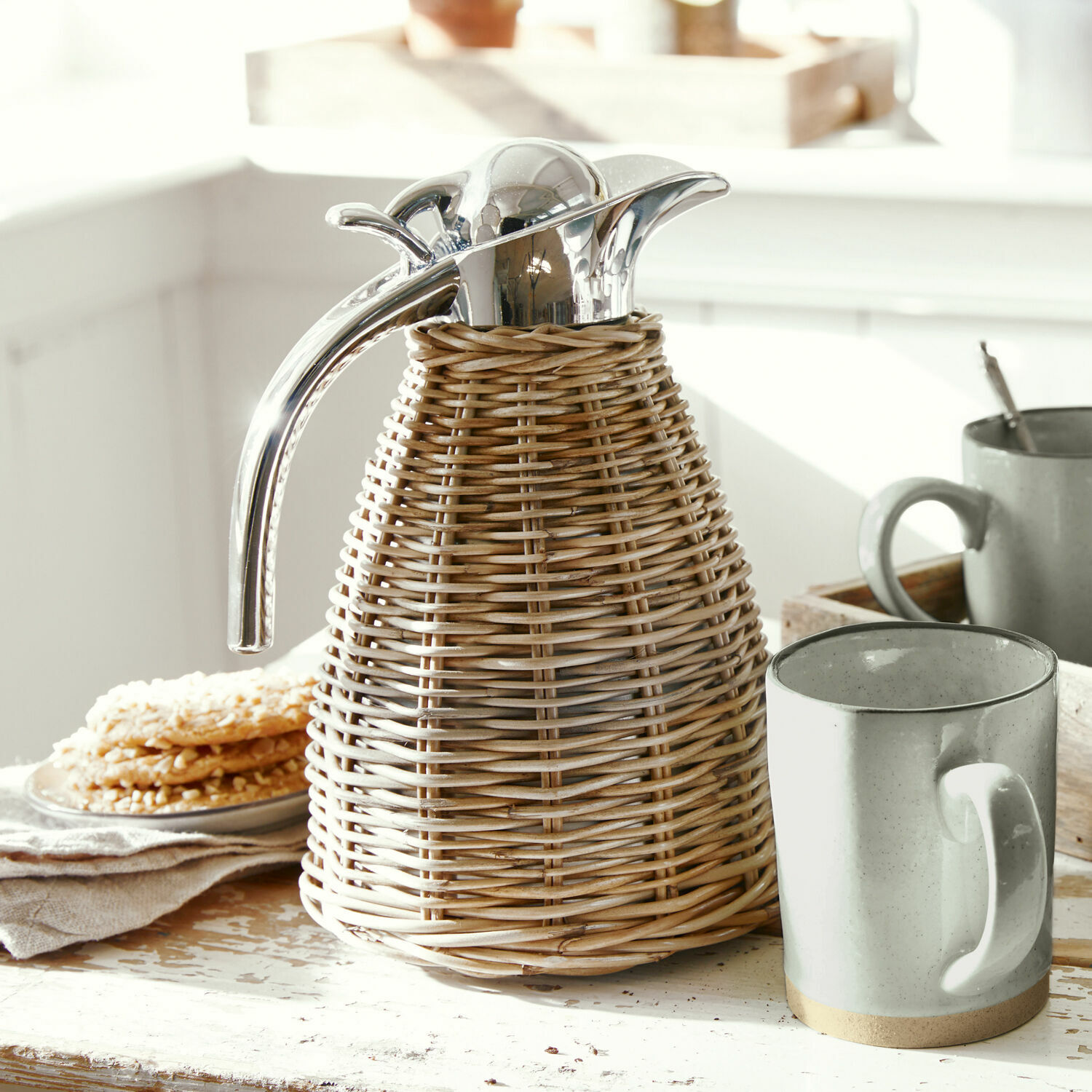 Pichet isotherme Senta Thermos en rotin avec bouchon et poignée en métal sur table rustique, ambiance chaleureuse