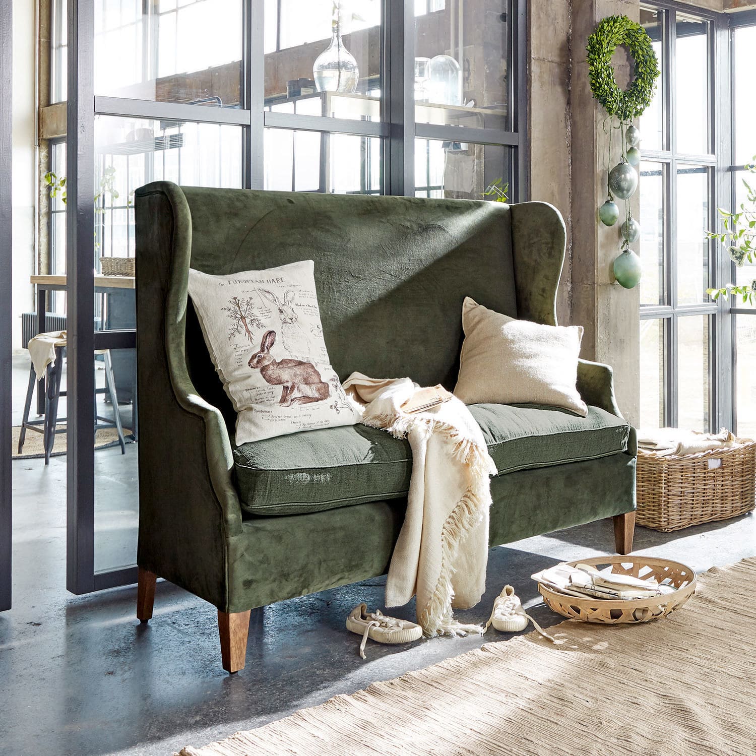 Canapé Ombra Canapé vert en velours avec coussins et plaid crème dans un intérieur lumineux et moderne avec grandes fenêtres