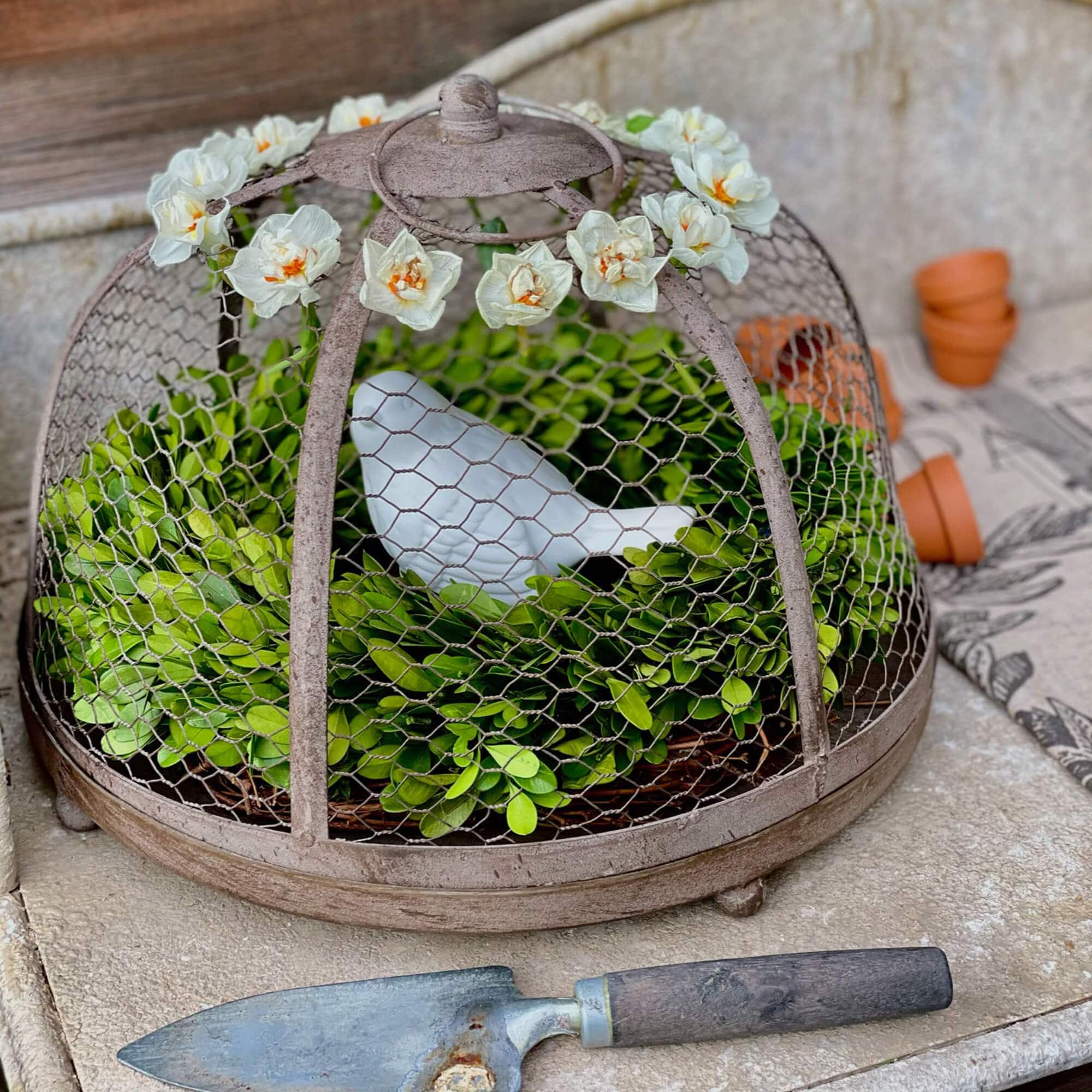 Décoration de jardin en métal avec feuillage vert et oiseau en céramique blanc sous cloche fleurie