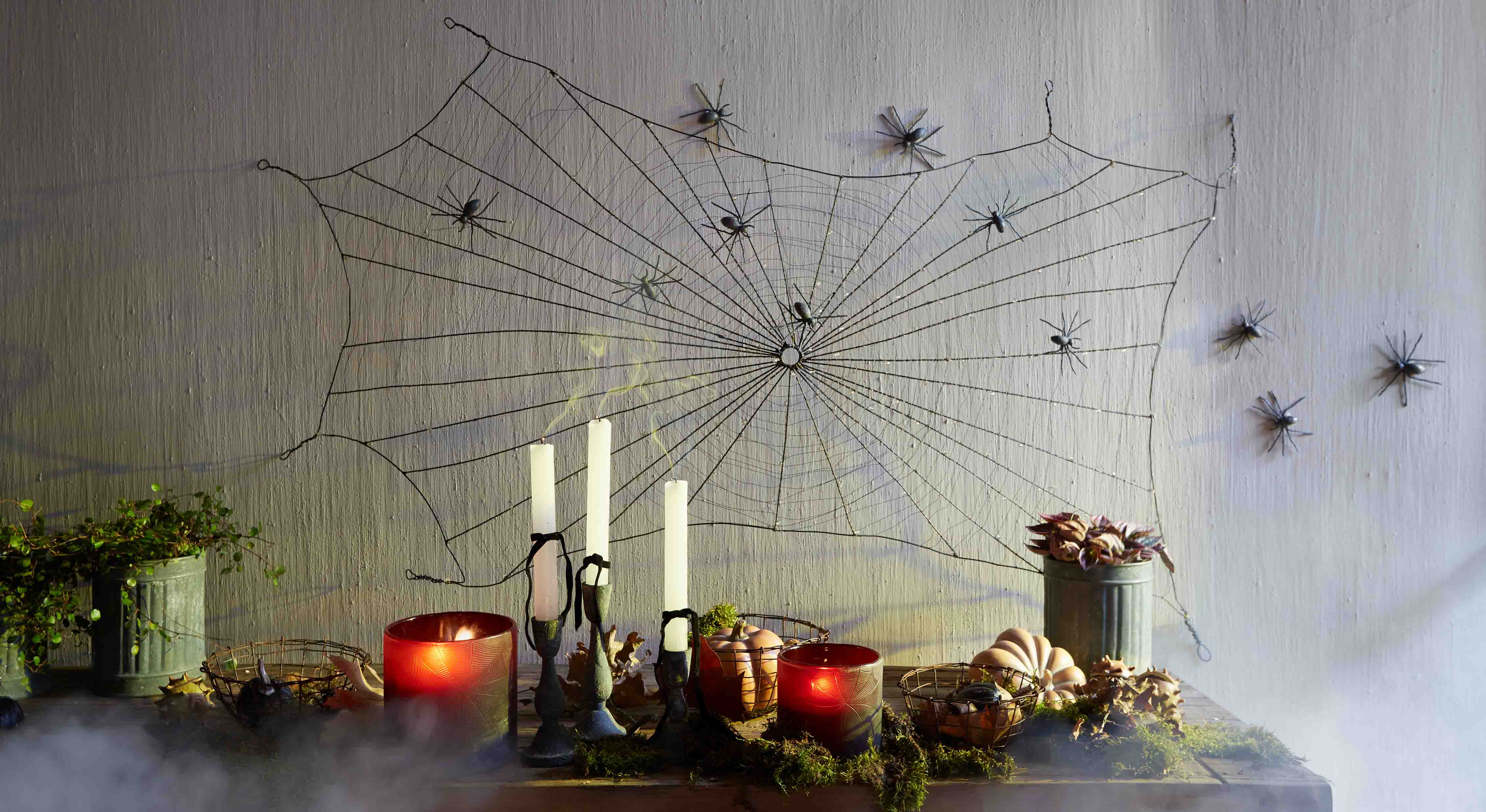 Décoration Halloween avec toile d'araignée noire et araignées en plastique sur le mur, bougies et citrouilles sur la table