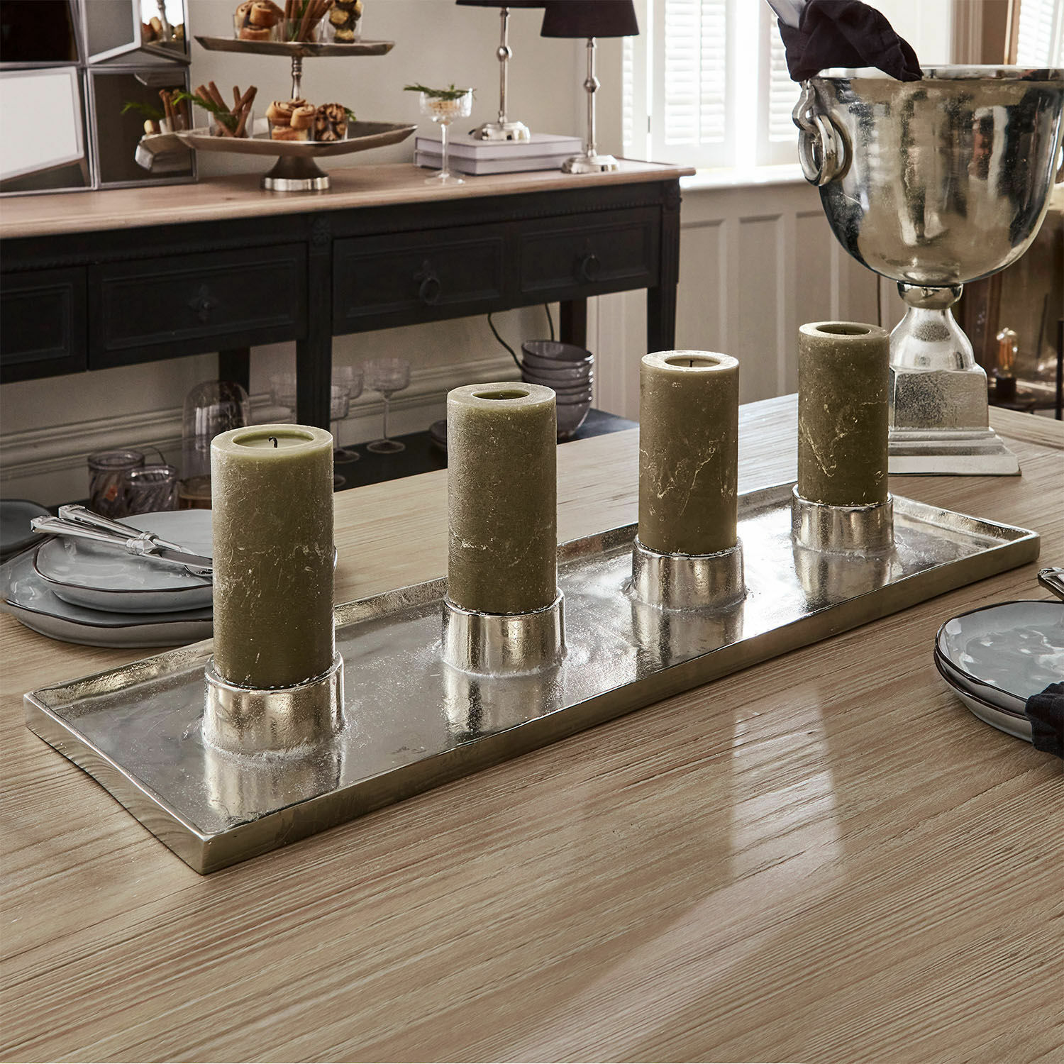 Ensemble de quatre bougies vertes sur un plateau en métal argenté sur une table en bois dans une salle à manger