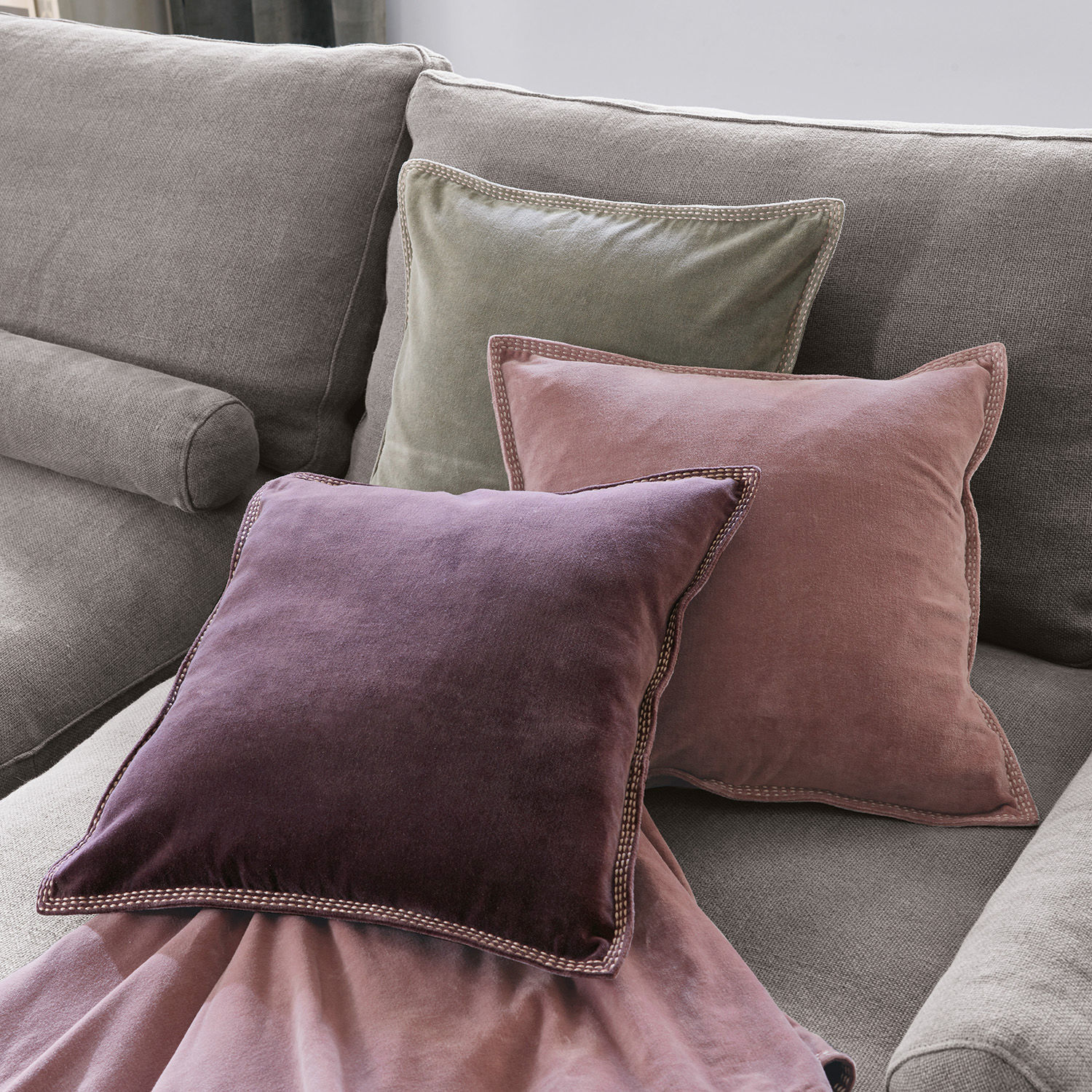 Lot de 3 coussins Allonnes Ensemble de trois coussins en velours violet, rose et vert sur un canapé gris clair
