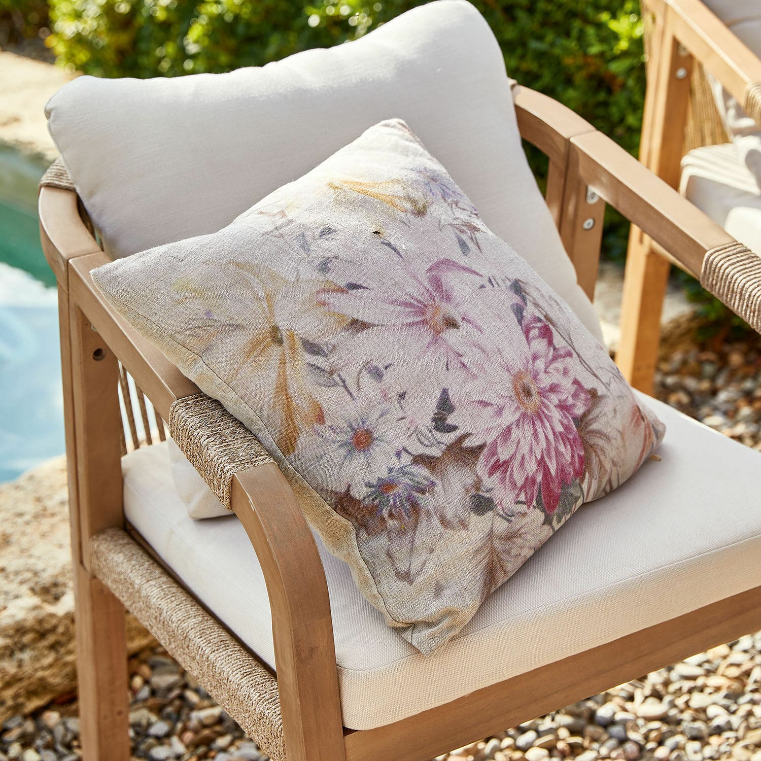 Housse de coussin Evie Coussin décoratif en lin beige avec motif floral posé sur un fauteuil en bois d'extérieur