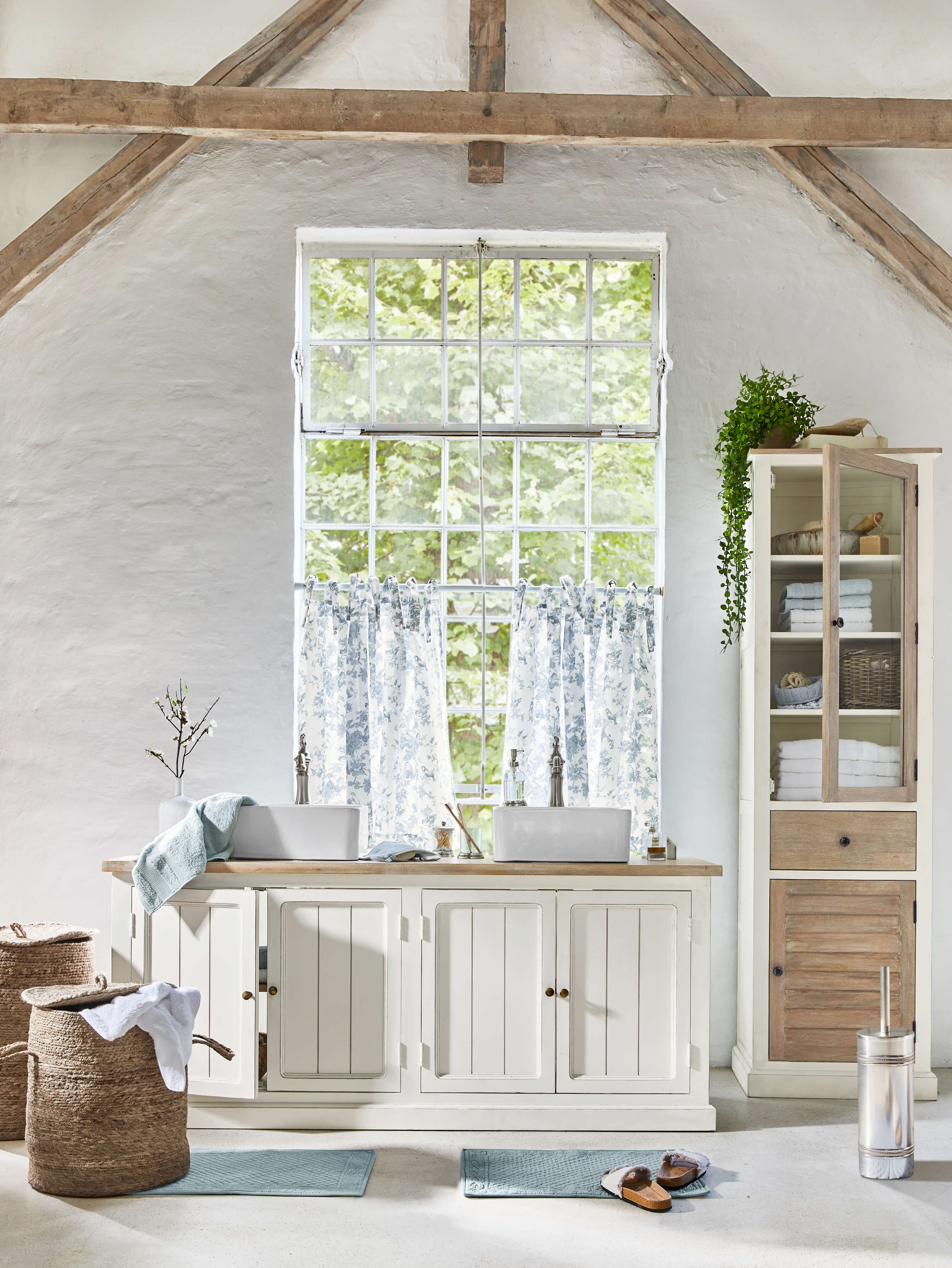 Meuble de salle de bain blanc en bois avec deux vasques et rideaux bleus dans un intérieur rustique