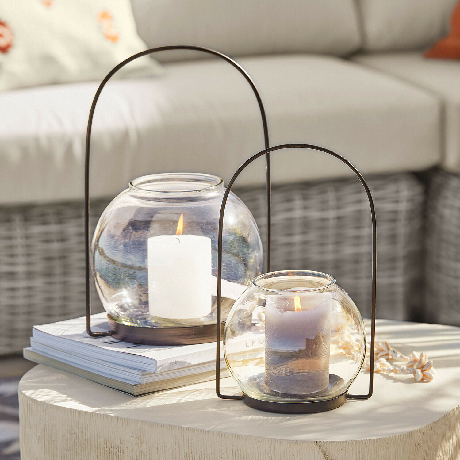 Deux lanternes en verre avec poignées métalliques et bougies allumées sur une table claire décorative