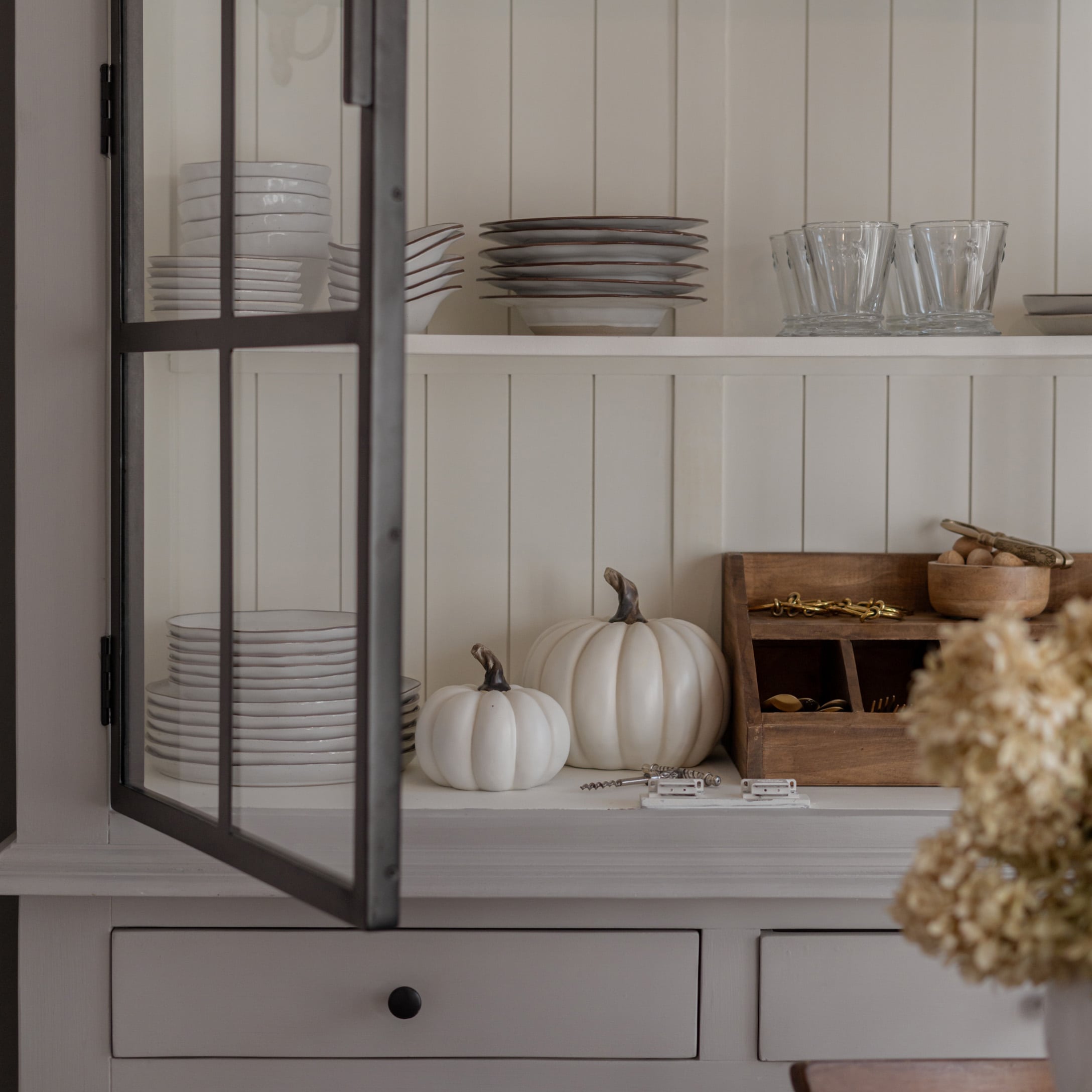 Assiettes blanches en céramique et verres sur étagère avec citrouilles blanches décoratives et organiseur en bois