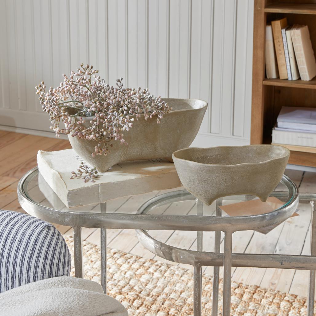Deux bols en céramique beige sur pieds posés sur une table en verre dans un intérieur lumineux et chaleureux