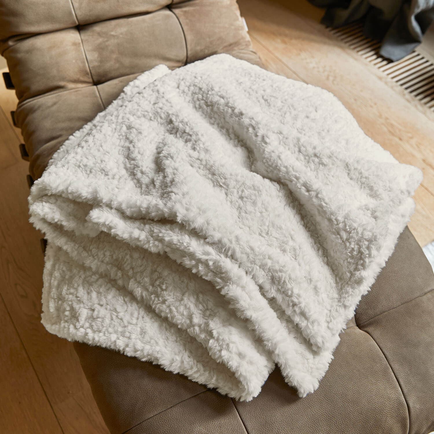 Plaid blanc doux en matière pelucheuse posé sur un fauteuil marron, parfait pour le salon