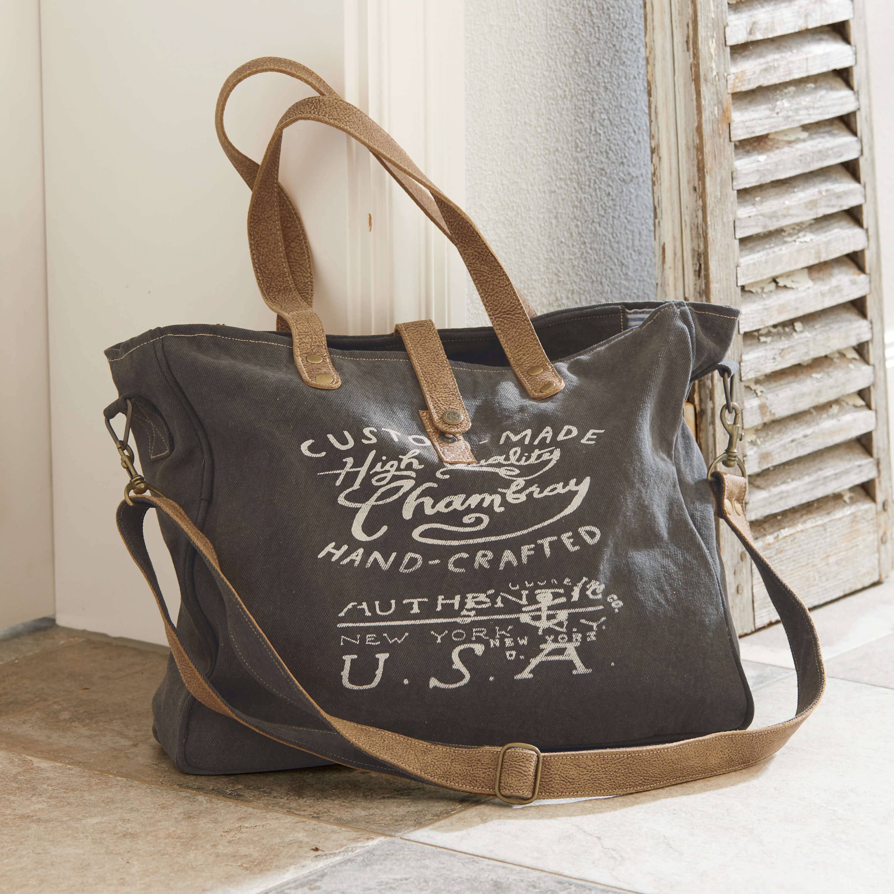 Sac de voyage en tissu gris foncé avec poignées en cuir marron et impression texte vintage