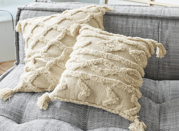Coussins décoratifs beiges avec franges et motifs géométriques sur canapé gris en tissu