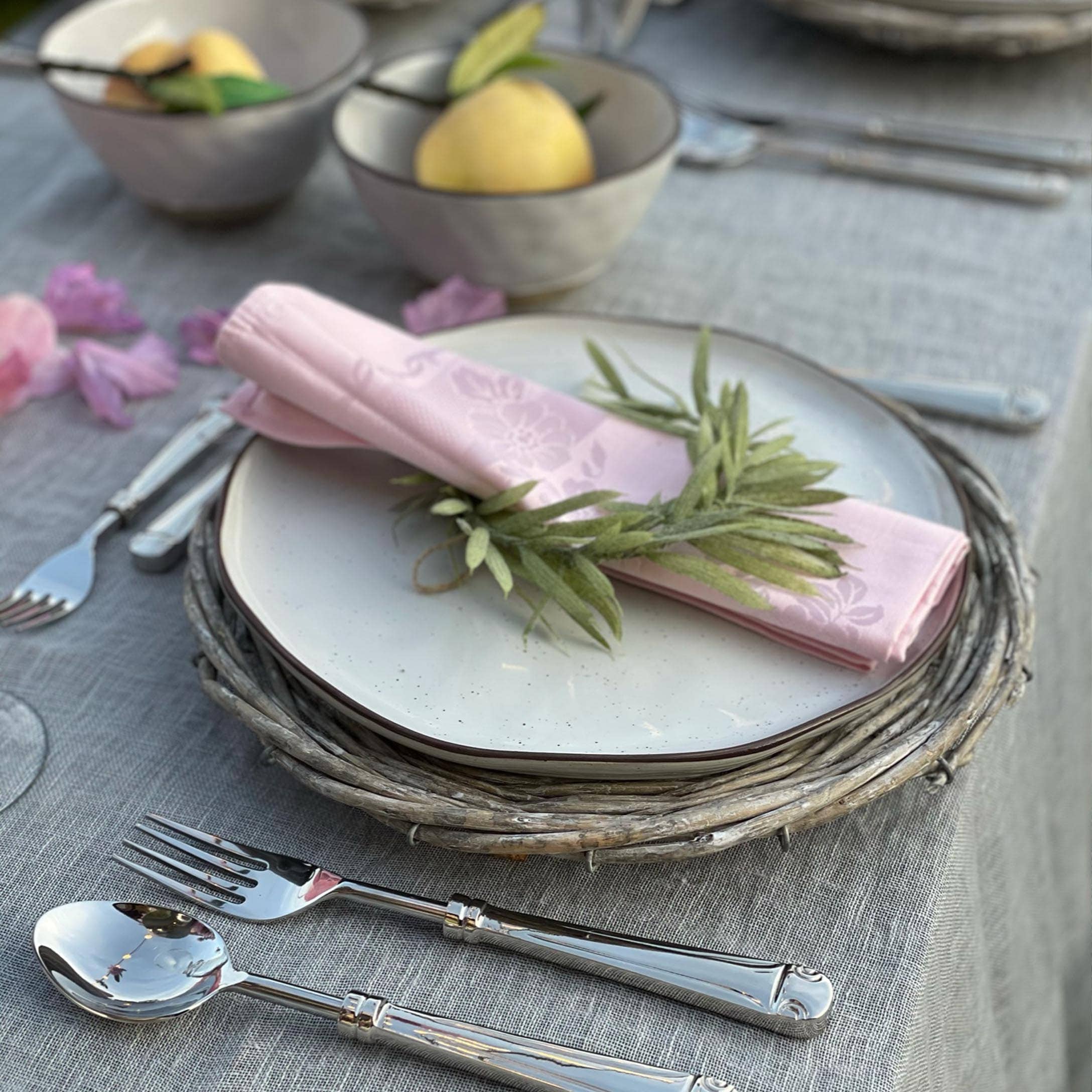 Service de table élégant avec assiette blanche sur dessous en osier et serviette rose décorée de feuilles vertes