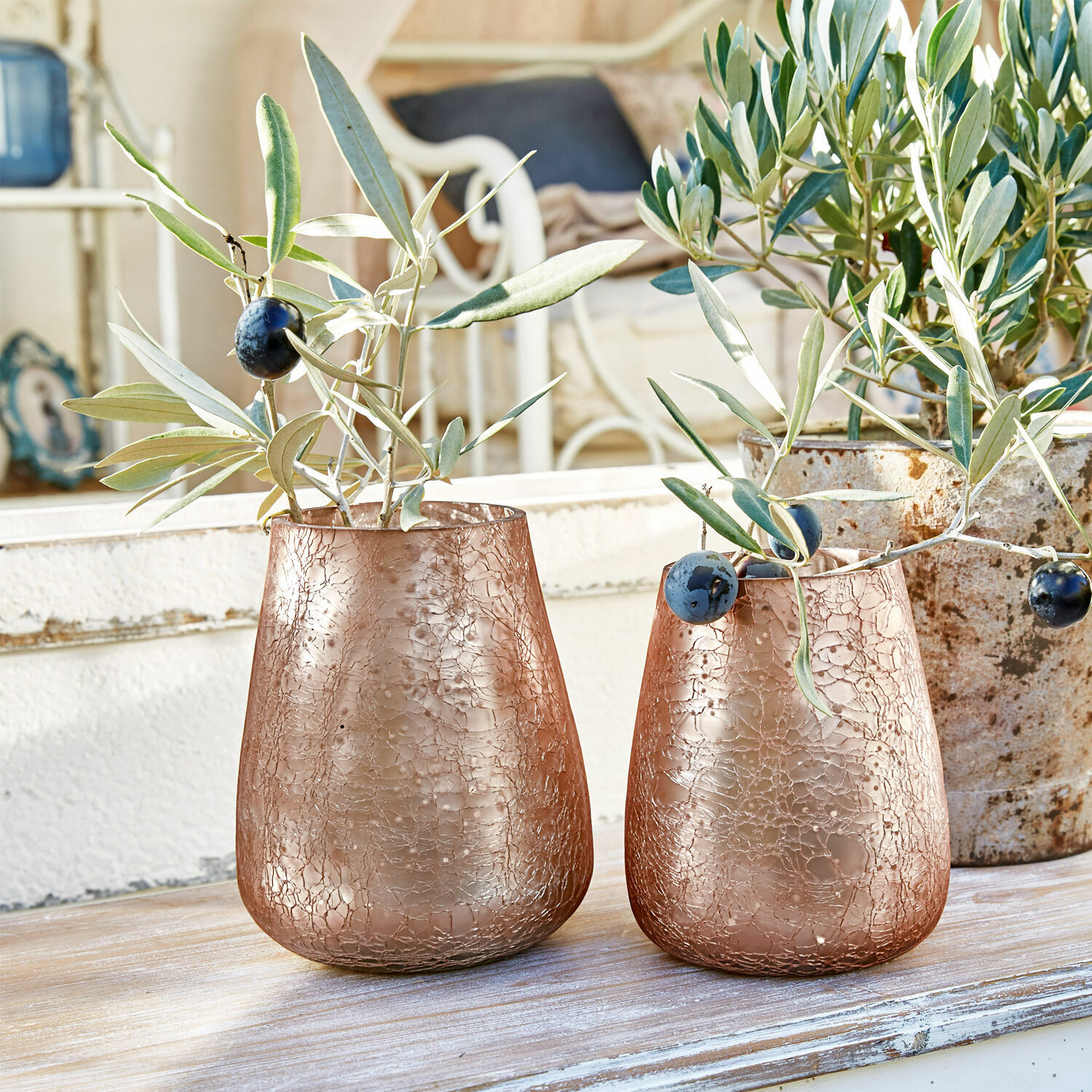 Lot de 2 photophores Chanut Deux vases en verre cuivré à texture craquelée avec branches d'olivier sur une table en bois