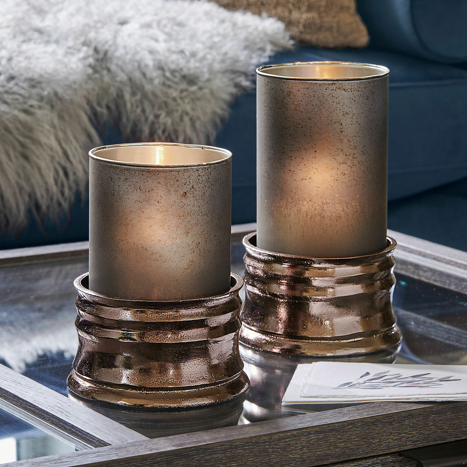 Lot de 2 photophores Eirun Deux photophores décoratifs en verre et métal cuivré sur une table en verre dans un salon moderne