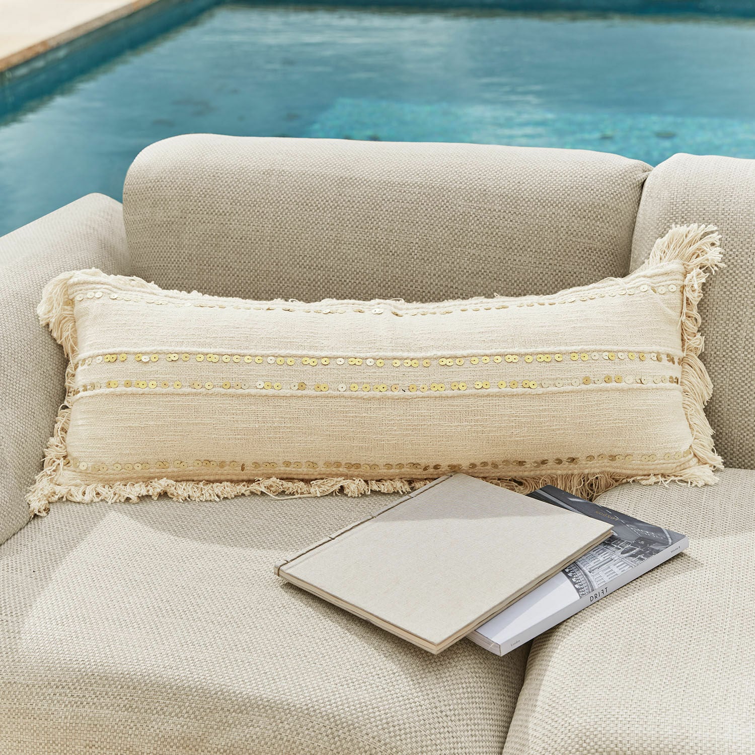 Coussin Rousseline Coussin décoratif beige allongé avec sequins et franges sur canapé clair près de la piscine