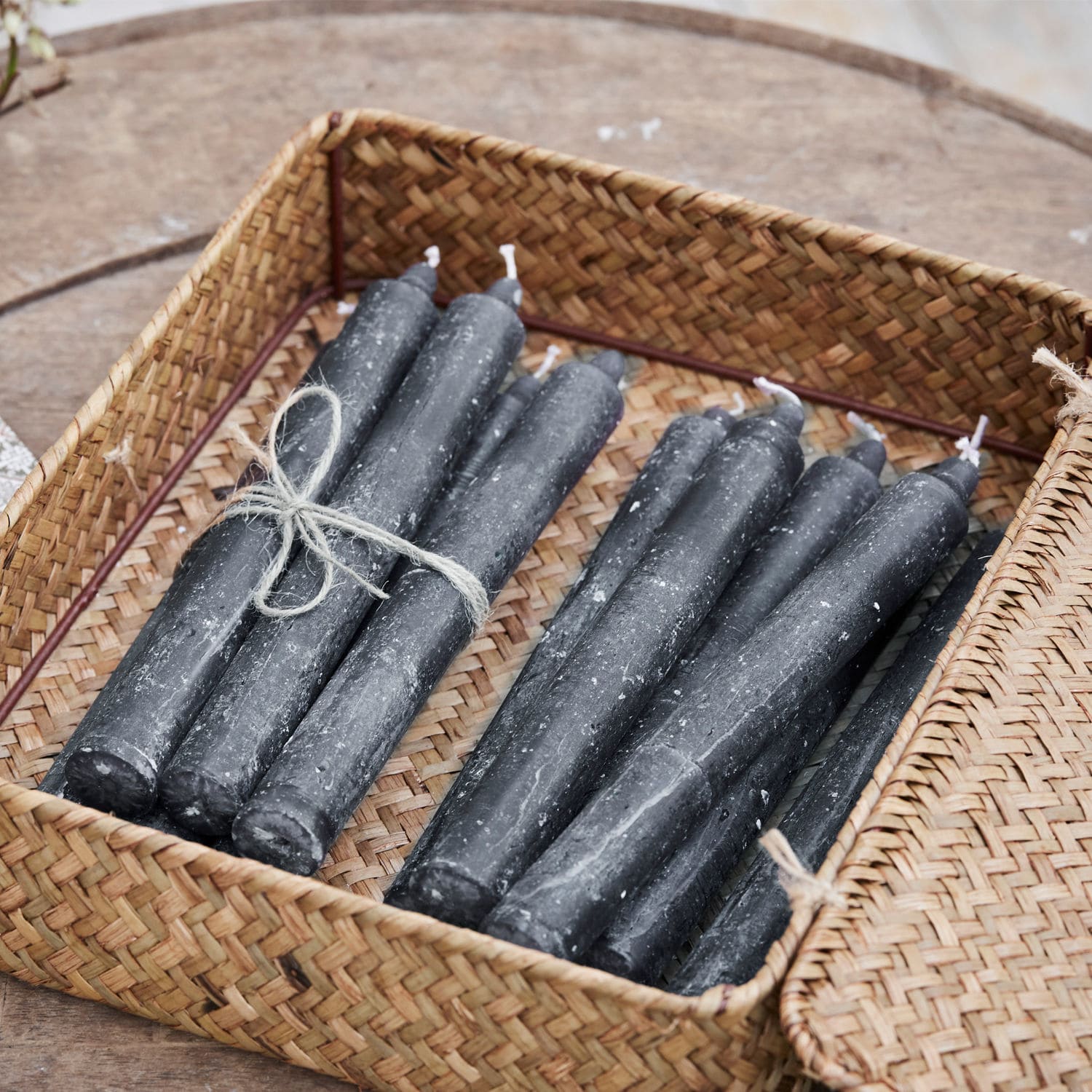 Lot de 12 bougies Bauceau Lot de bougies noires en cire dans un panier en osier sur une table en bois