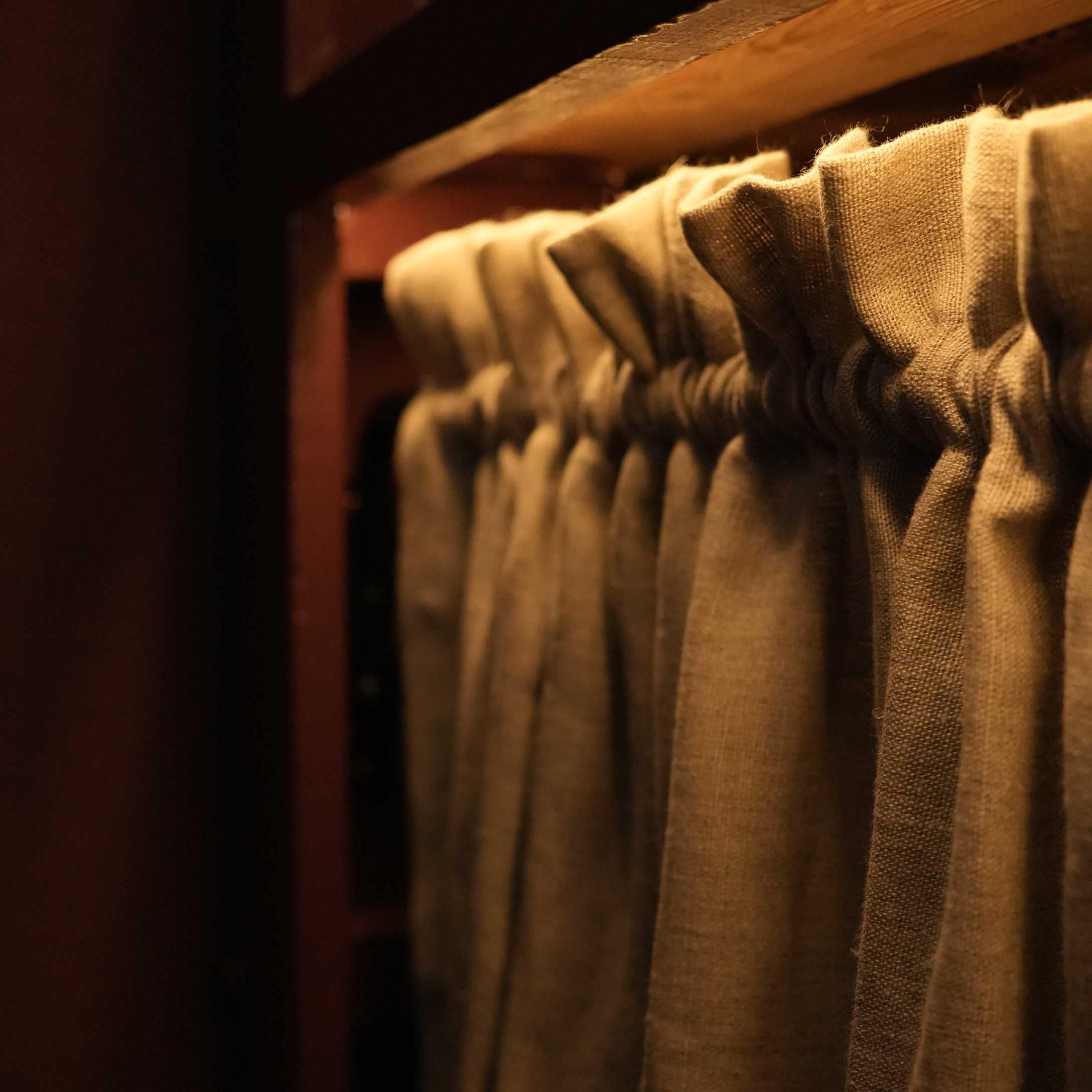 Rideau en lin beige plissé sur tringle en bois éclairé par une lumière chaude