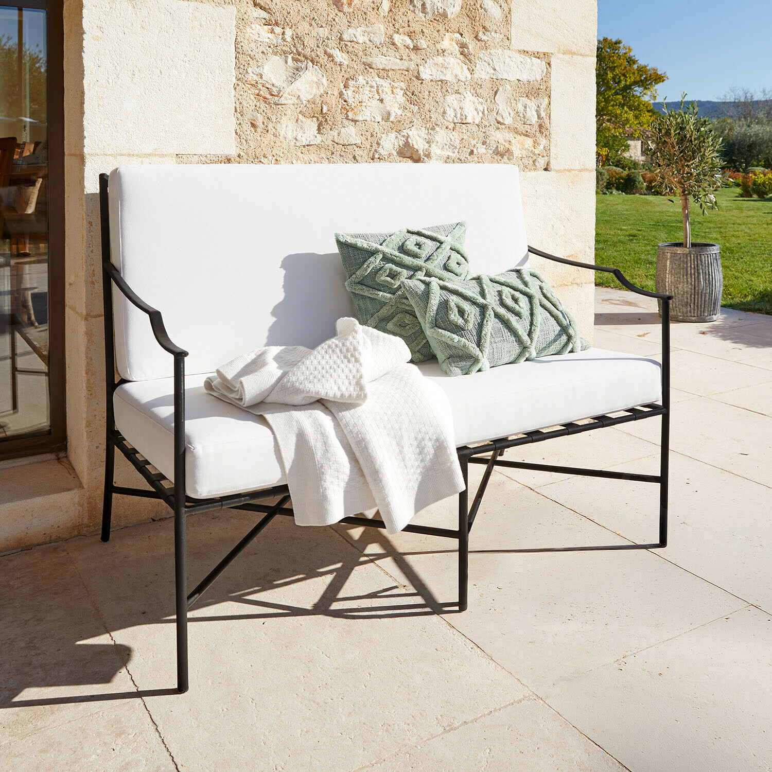 Banc de jardin en métal blanc avec coussins doux et coussins décoratifs verts sur la terrasse ensoleillée