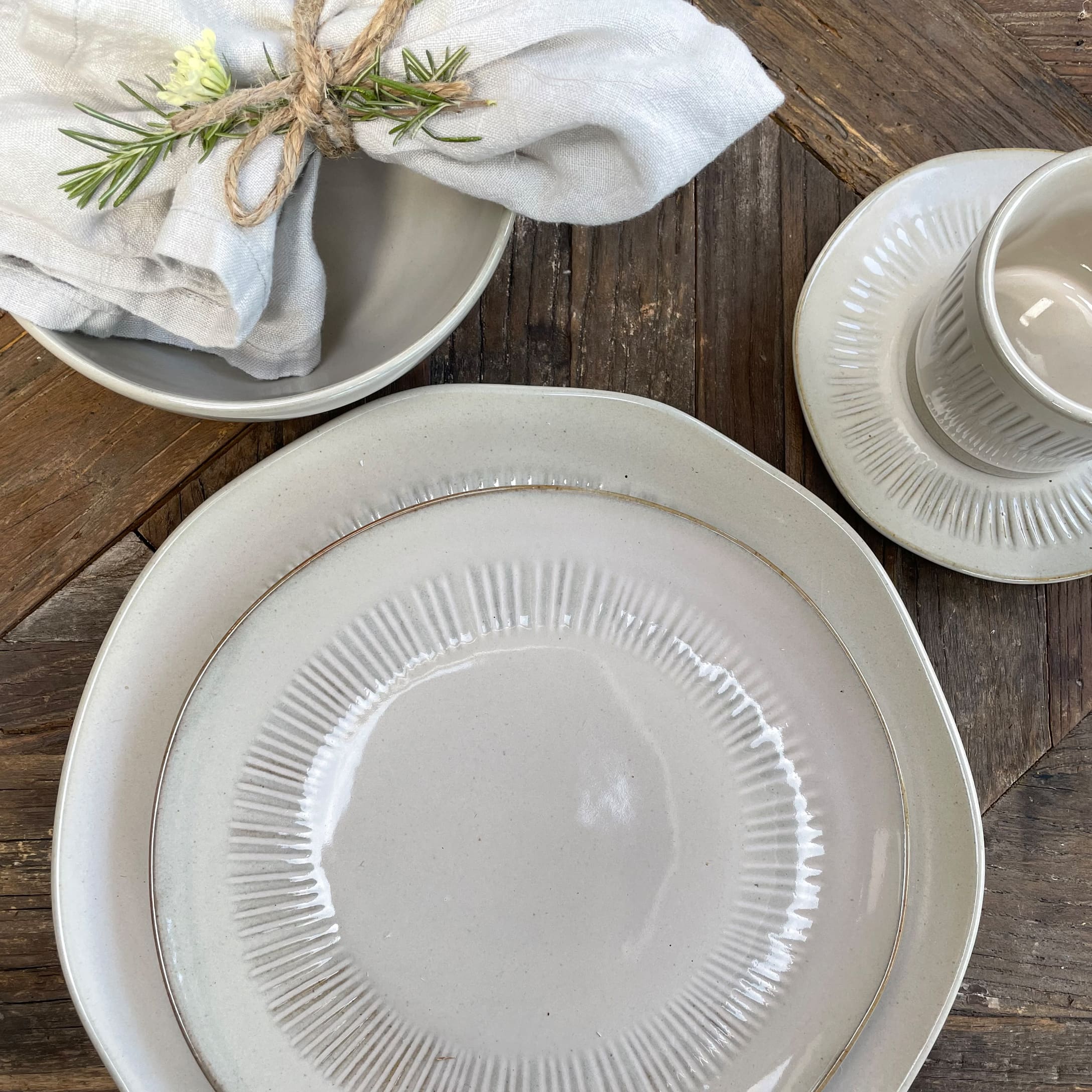 Ensemble d'assiettes et tasse en céramique crème sur table en bois avec serviette en lin et romarin