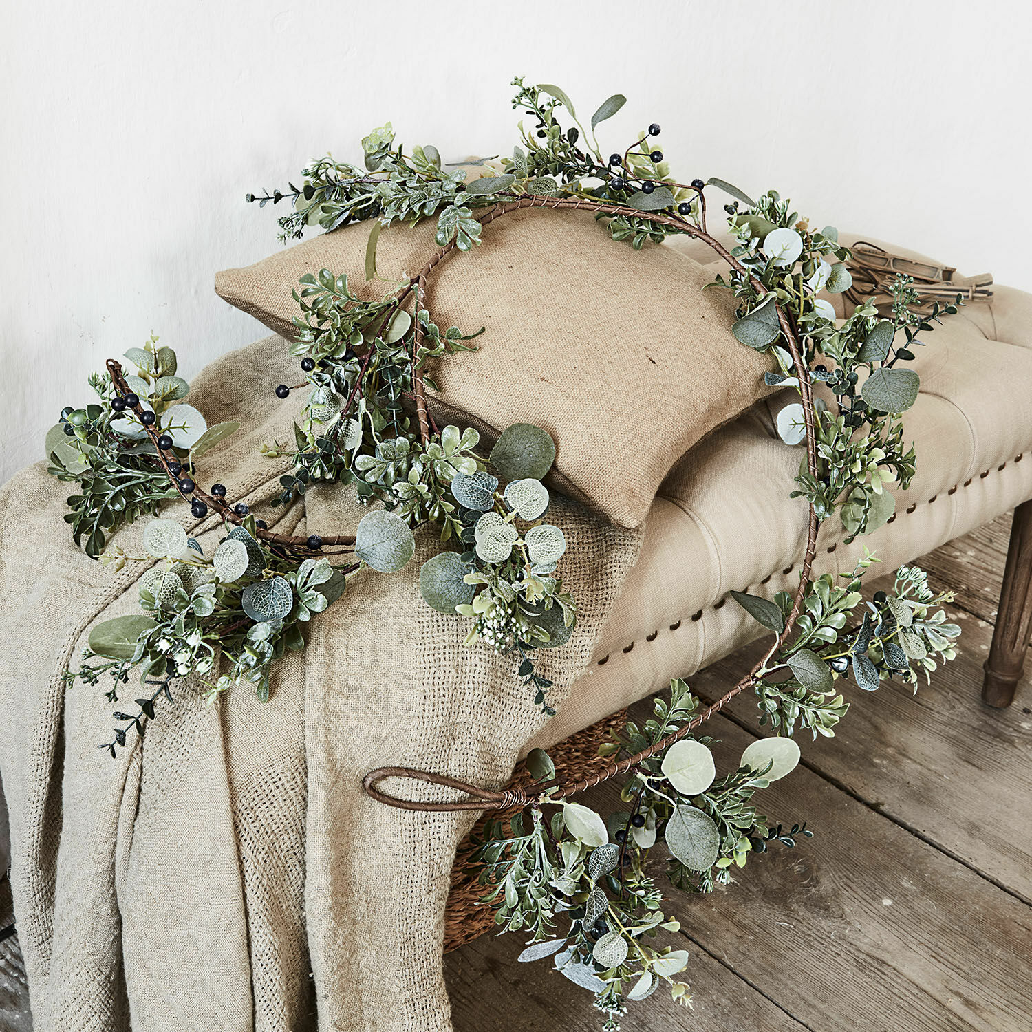 Guirlande Grand Couronne décorative en feuillage vert et baies noires posée sur tissu beige et banc en bois