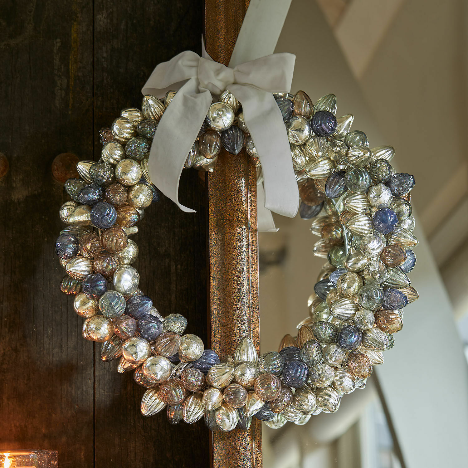 Couronne Azélisse Couronne décorative en boules de verre colorées avec un nœud blanc accrochée à une porte en bois