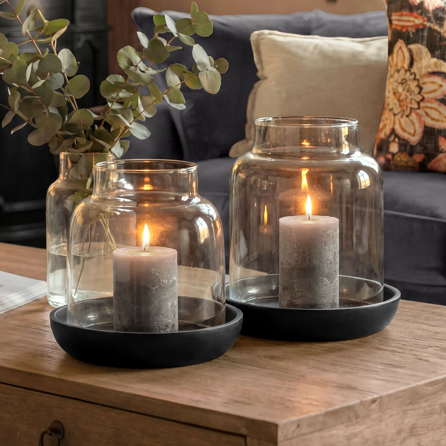 Lot de 2 photophores Venturio Bougies grises dans des lanternes en verre avec socles noirs sur une table en bois dans un salon
