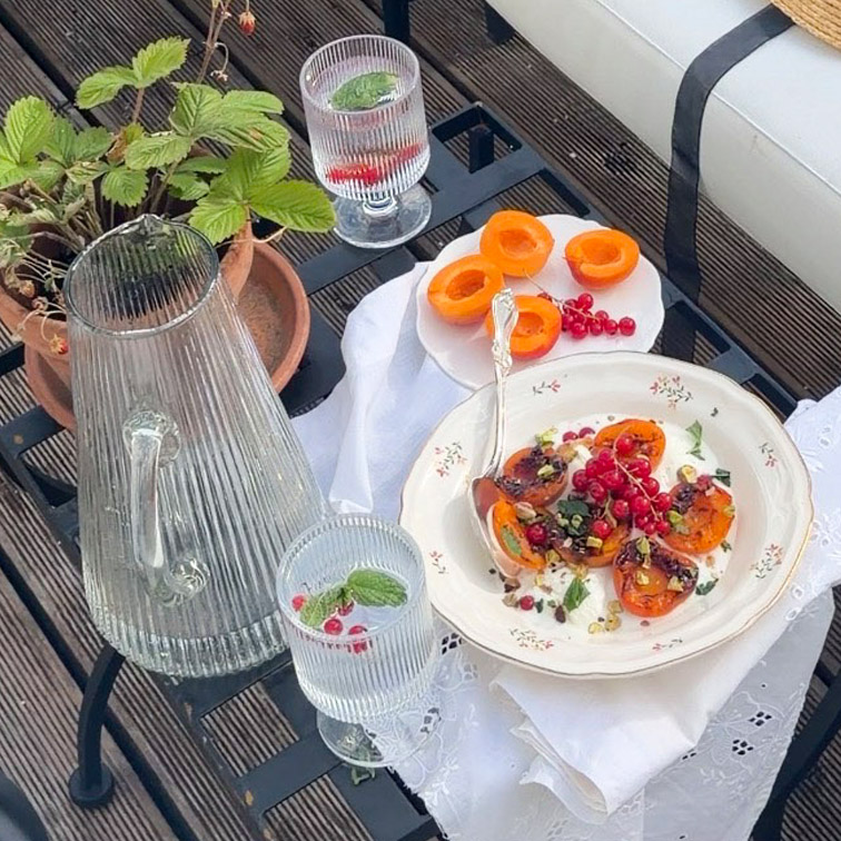 Carafe et deux verres en verre avec eau à la menthe sur table avec assiettes d'abricots et groseilles rouges