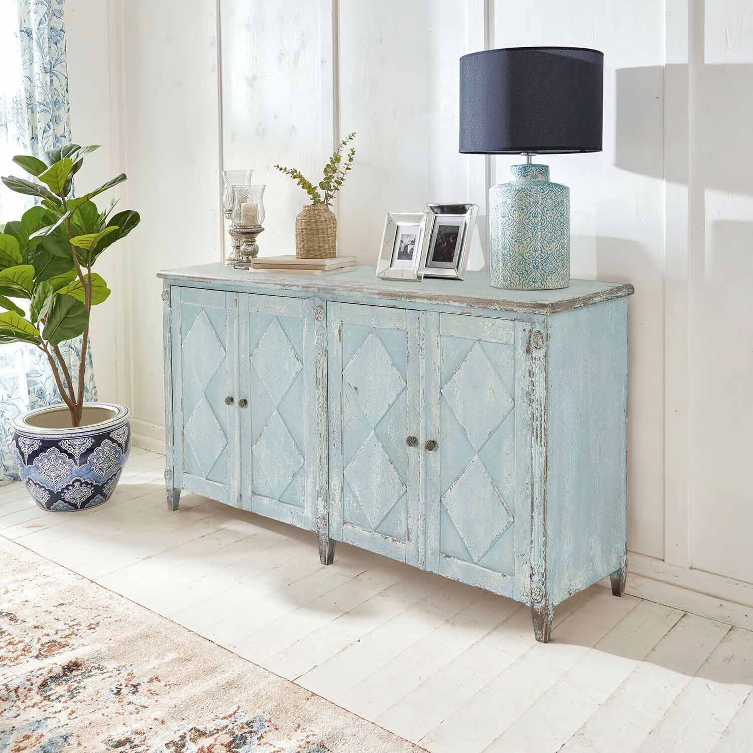 Buffet en bois bleu patiné style vintage dans une pièce claire avec lampe et plante décorative