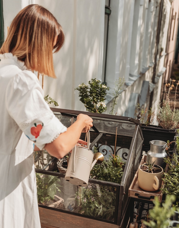 Femme arrosant des plantes dans une petite serre en verre sur un balcon ensoleillé