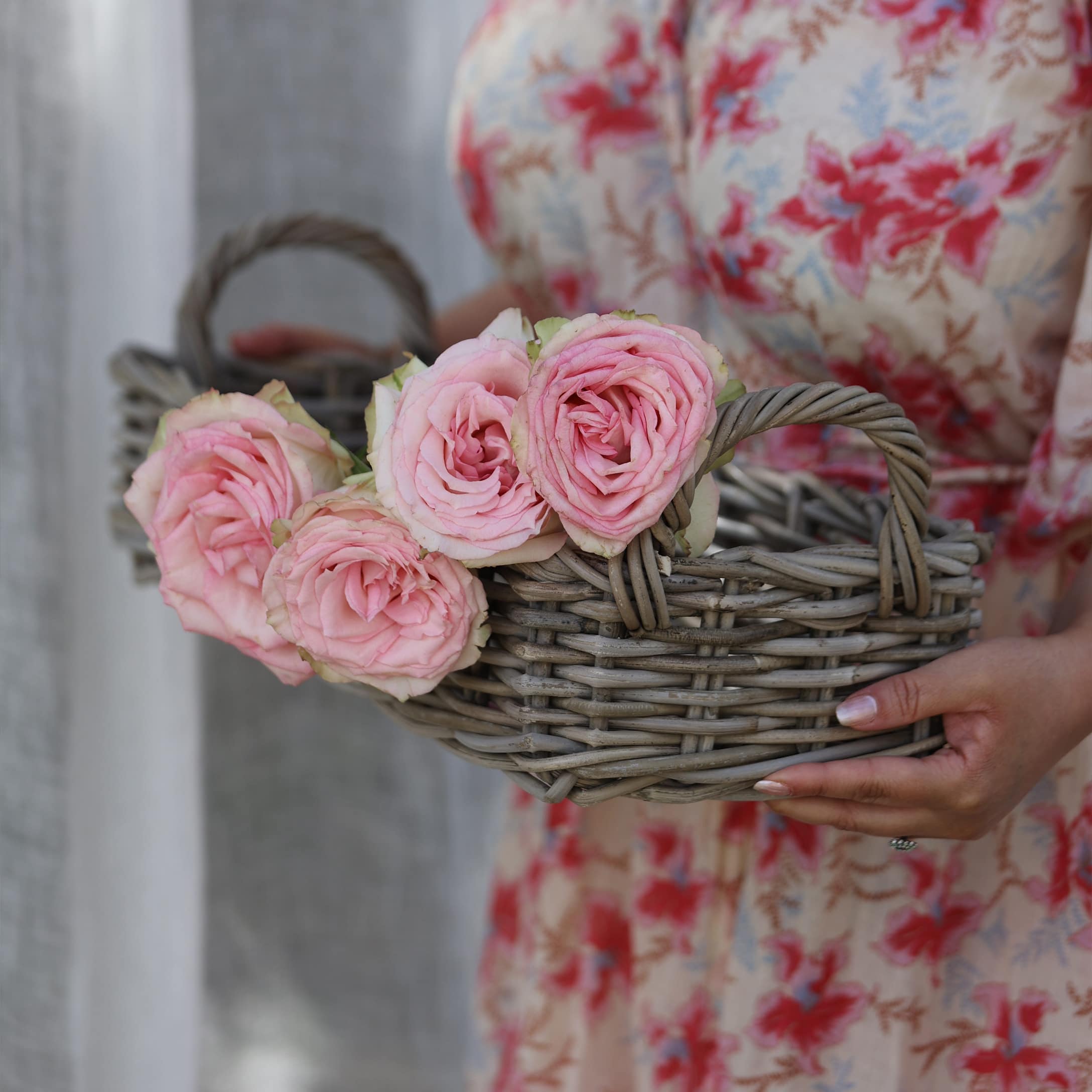 Petit panier en osier gris avec roses roses tenu par une personne en robe fleurie