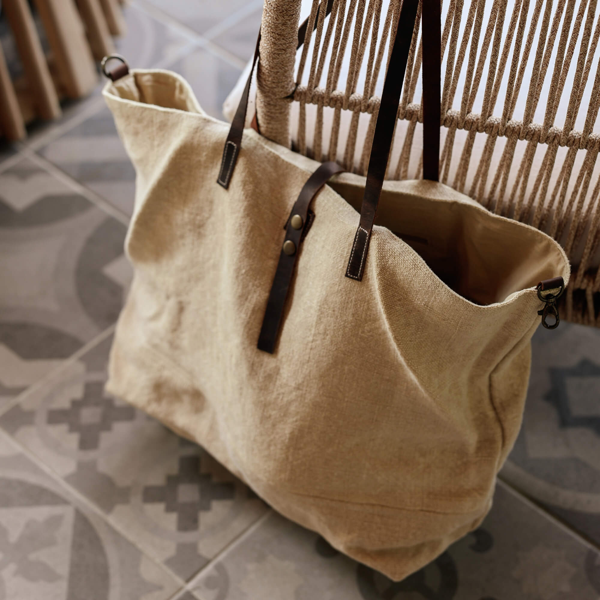 Sac beige en tissu avec poignées en cuir marron foncé posé sur un sol carrelé à motifs