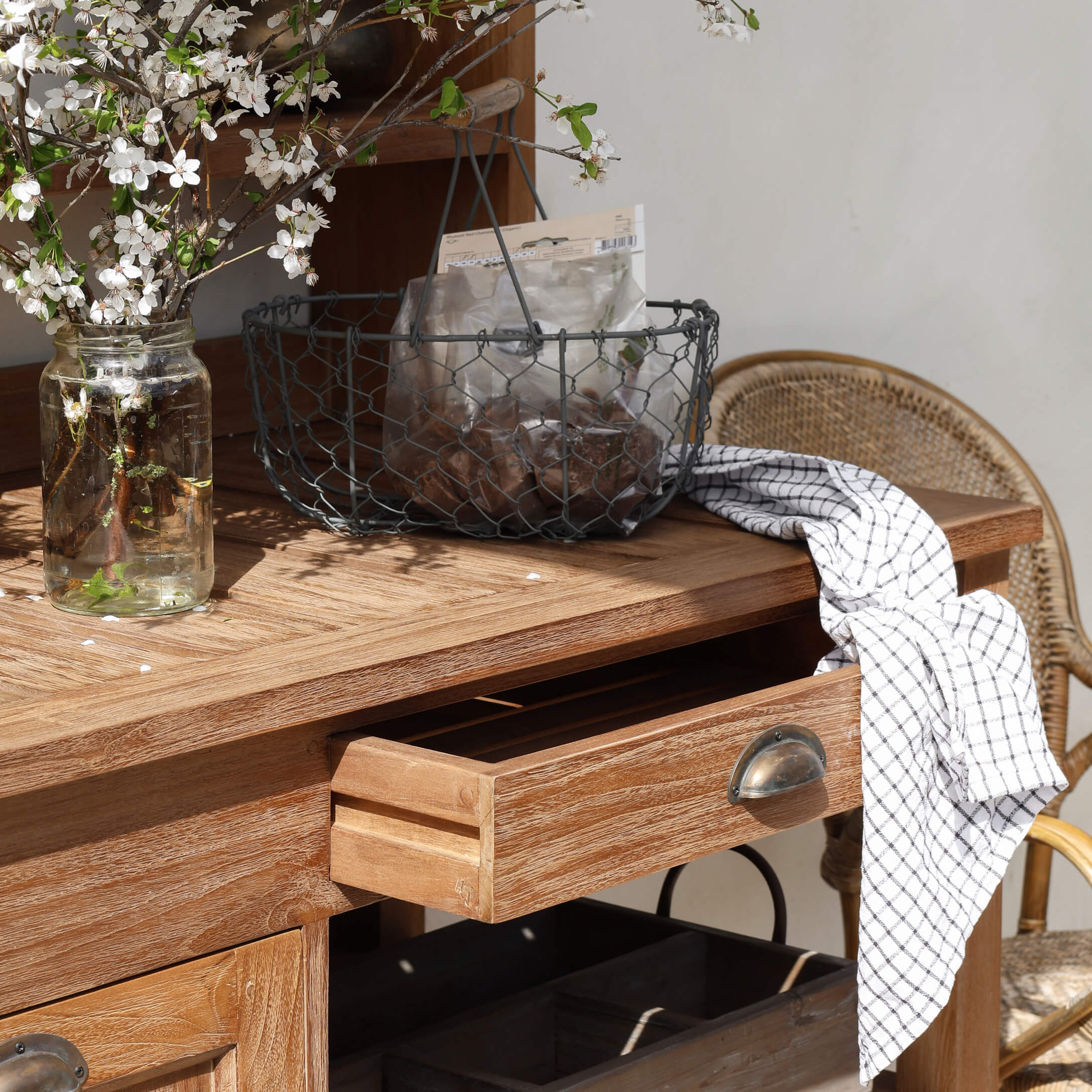 Table en bois avec tiroir ouvert, panier en métal et torchon blanc à carreaux sur le dessus