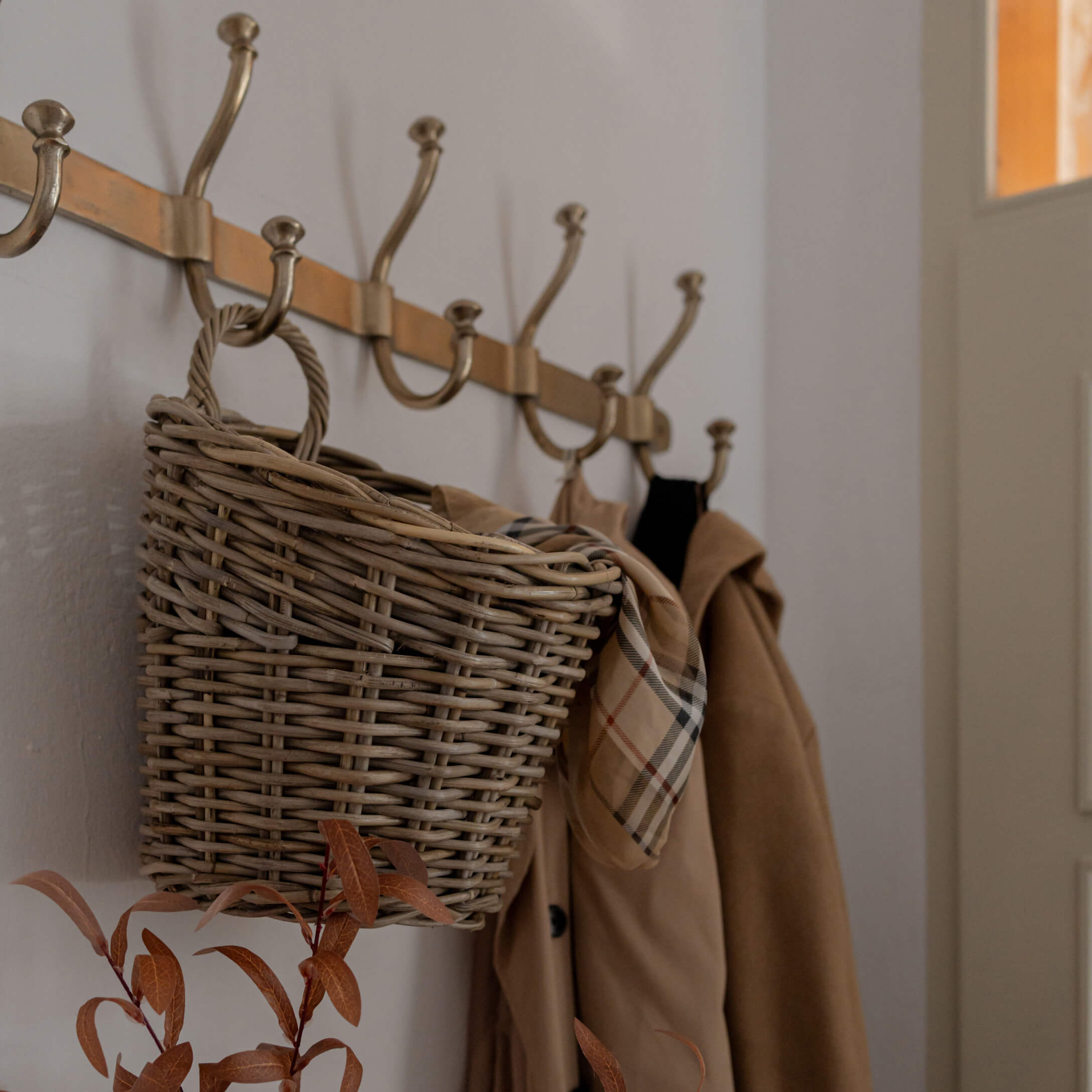 Panier en osier suspendu à un porte-manteau en laiton avec manteau beige et écharpe à carreaux