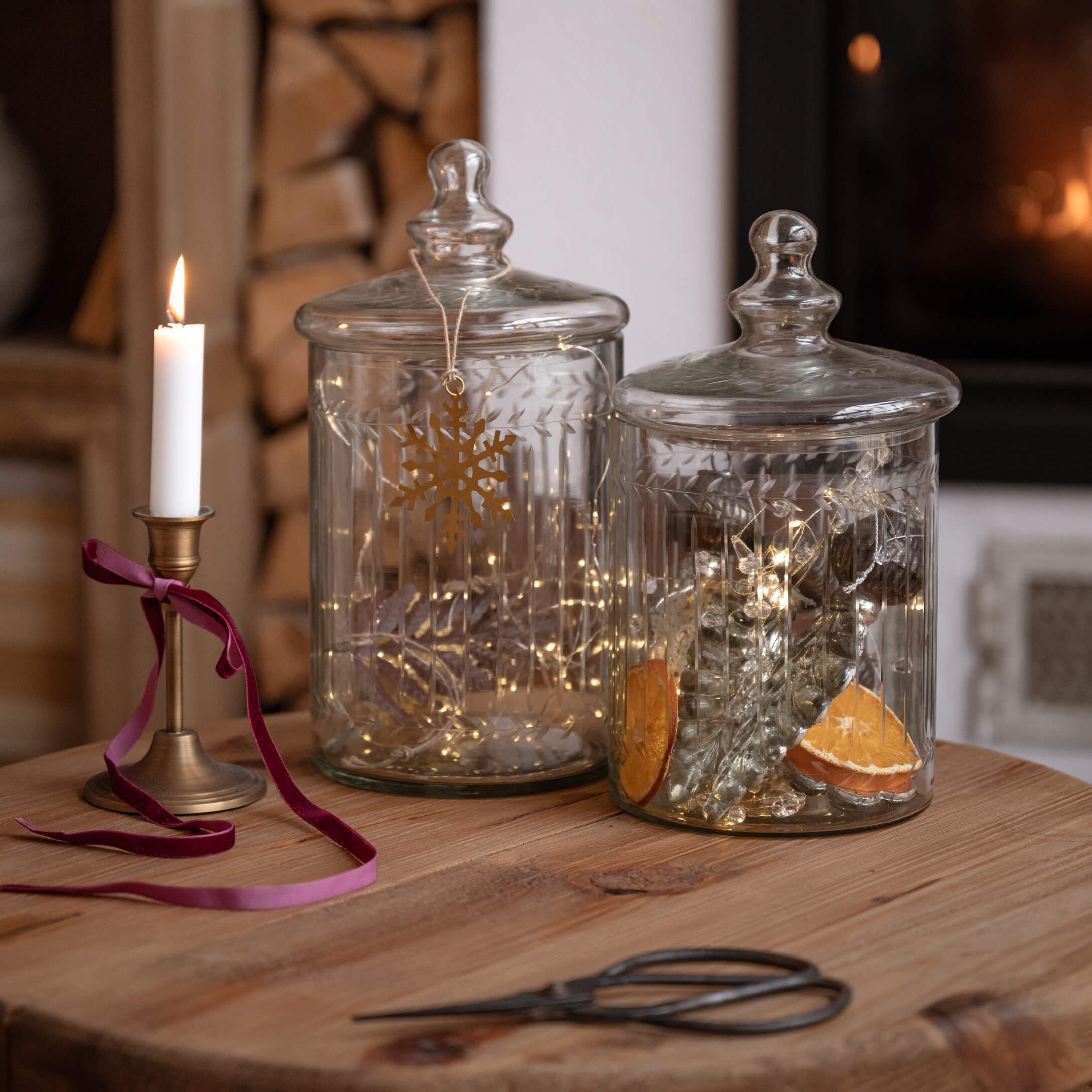 Bocaux en verre transparent avec couvercles sur table en bois, décorations lumineuses et bougie allumée