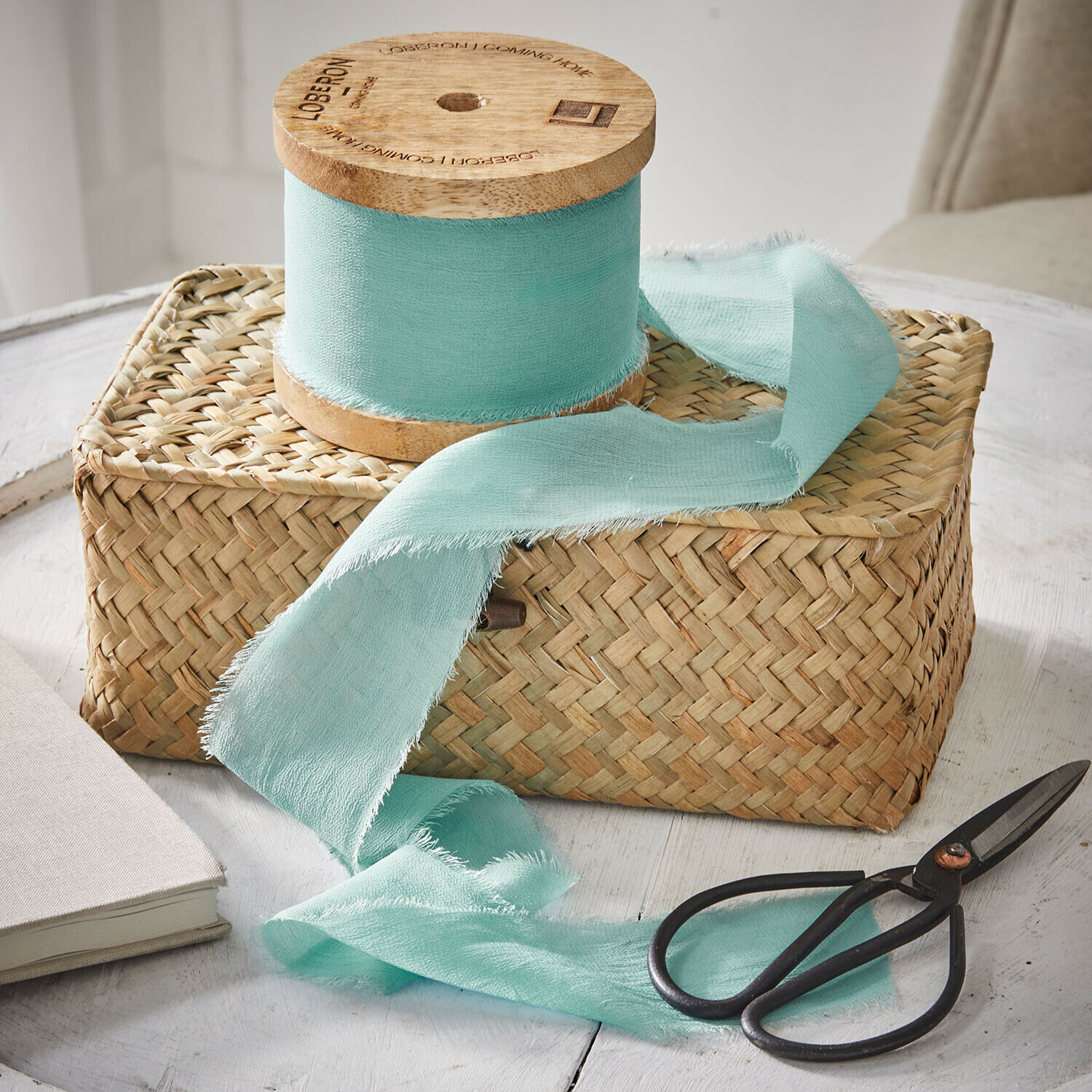 Ruban Lunebrook Ruban en coton vert menthe sur bobine en bois posé sur panier tressé avec ciseaux vintage