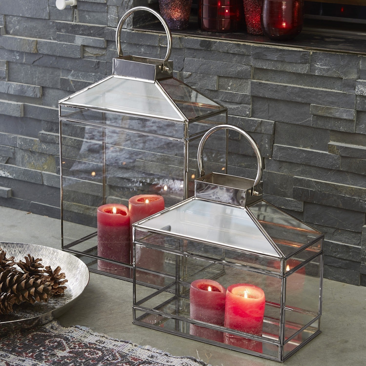 Lot de 2 lanternes Francesca Lanterne en verre avec cadre métallique et bougies rouges devant un mur en pierre, décoration intérieure