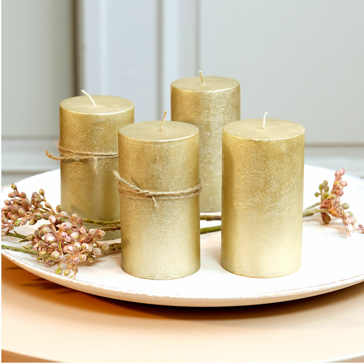 Lot de 4 bougies Braga Ensemble de quatre bougies décoratives dorées sur une assiette blanche avec des branches décoratives