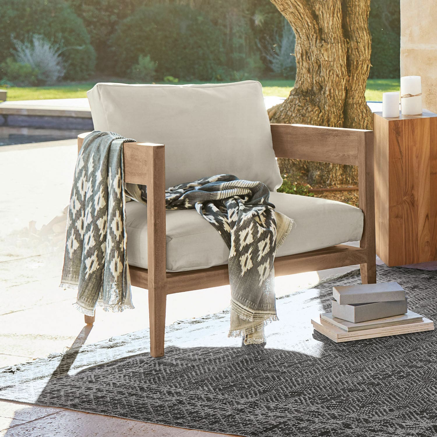 Fauteuil Courtelevant Fauteuil avec coussins beige clair et structure en bois, plaid gris à motifs posé dessus en extérieur