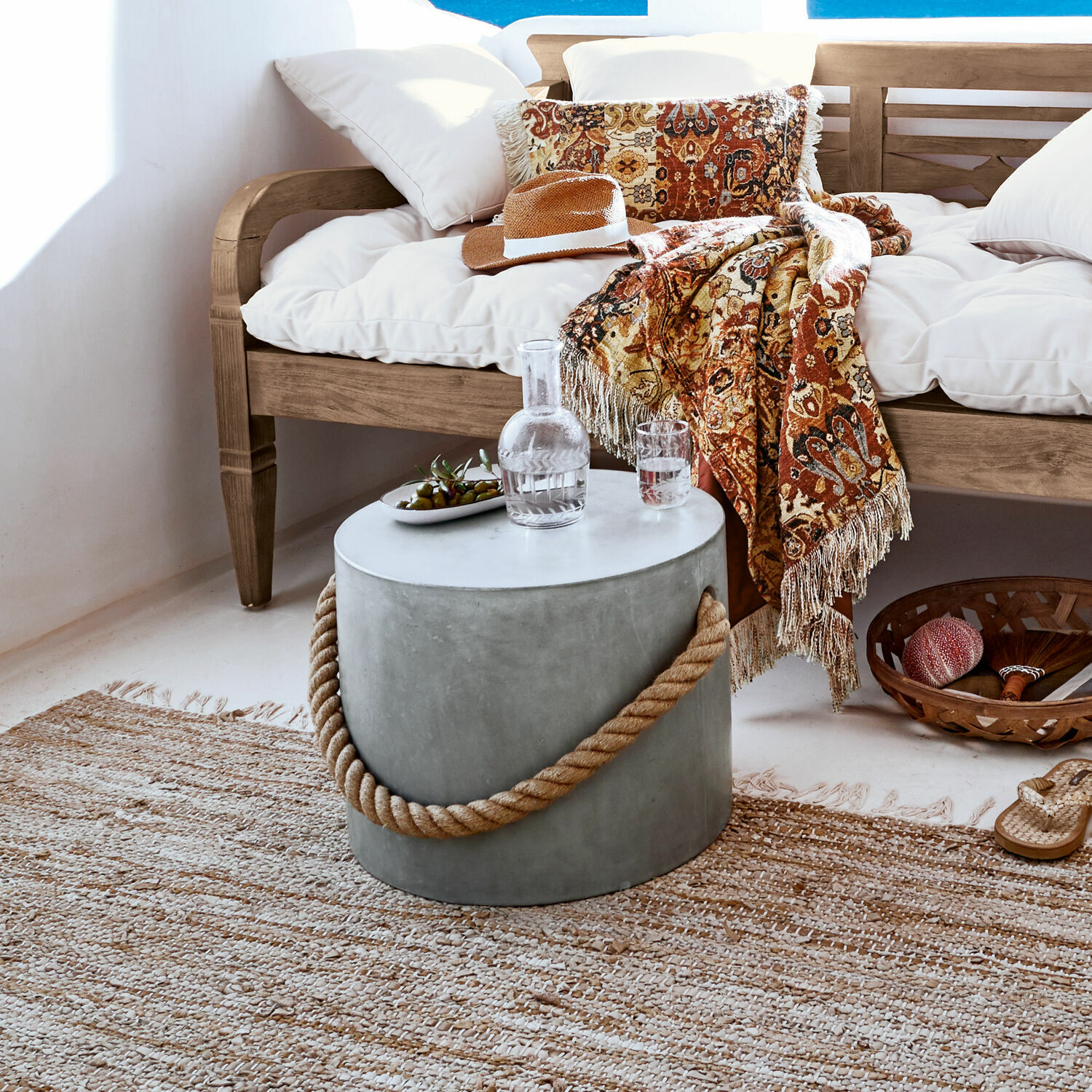 Pouf Kaedi Table ronde en béton avec poignée en corde dans un salon naturel avec canapé en bois et plaid décoratif
