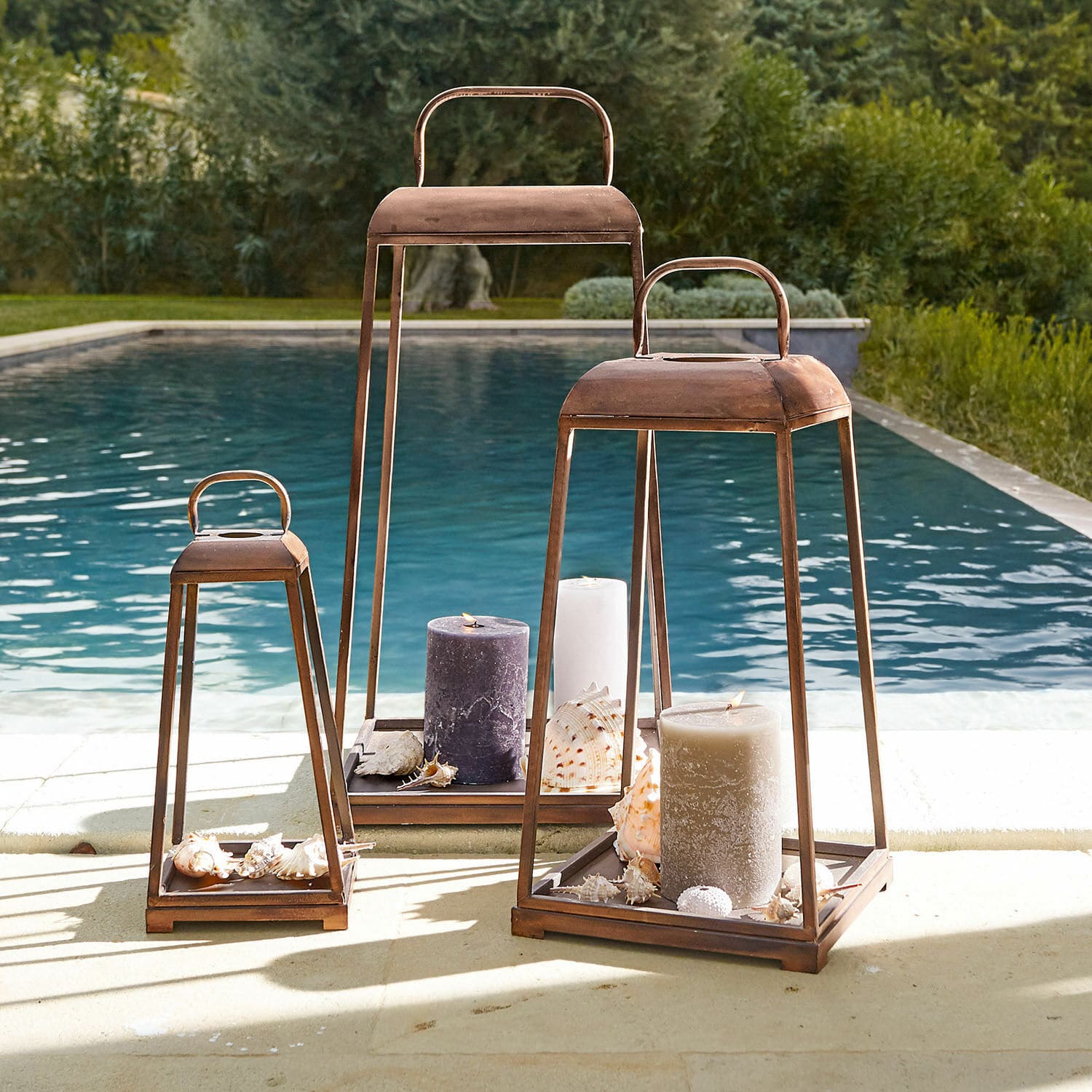 Lot de 3 lanternes Martie Trois lanternes en métal rouillé avec grandes bougies et coquillages au bord de la piscine