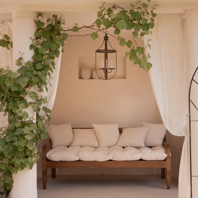 Canapé en bois avec coussins crème dans un intérieur lumineux avec plantes vertes et lampe suspendue