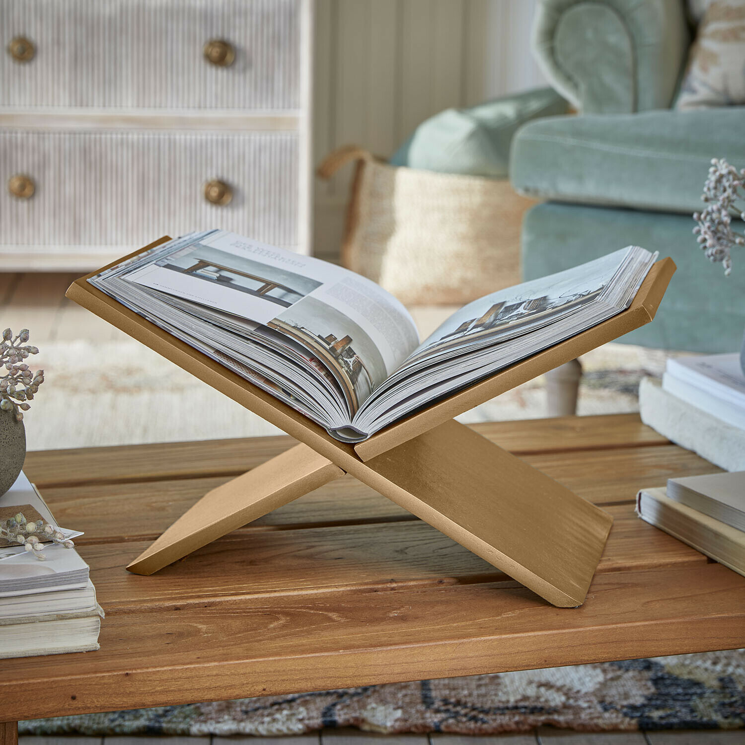 Porte-revues Rashira Support à livre doré en bois sur une table basse dans un salon confortable avec canapé vert