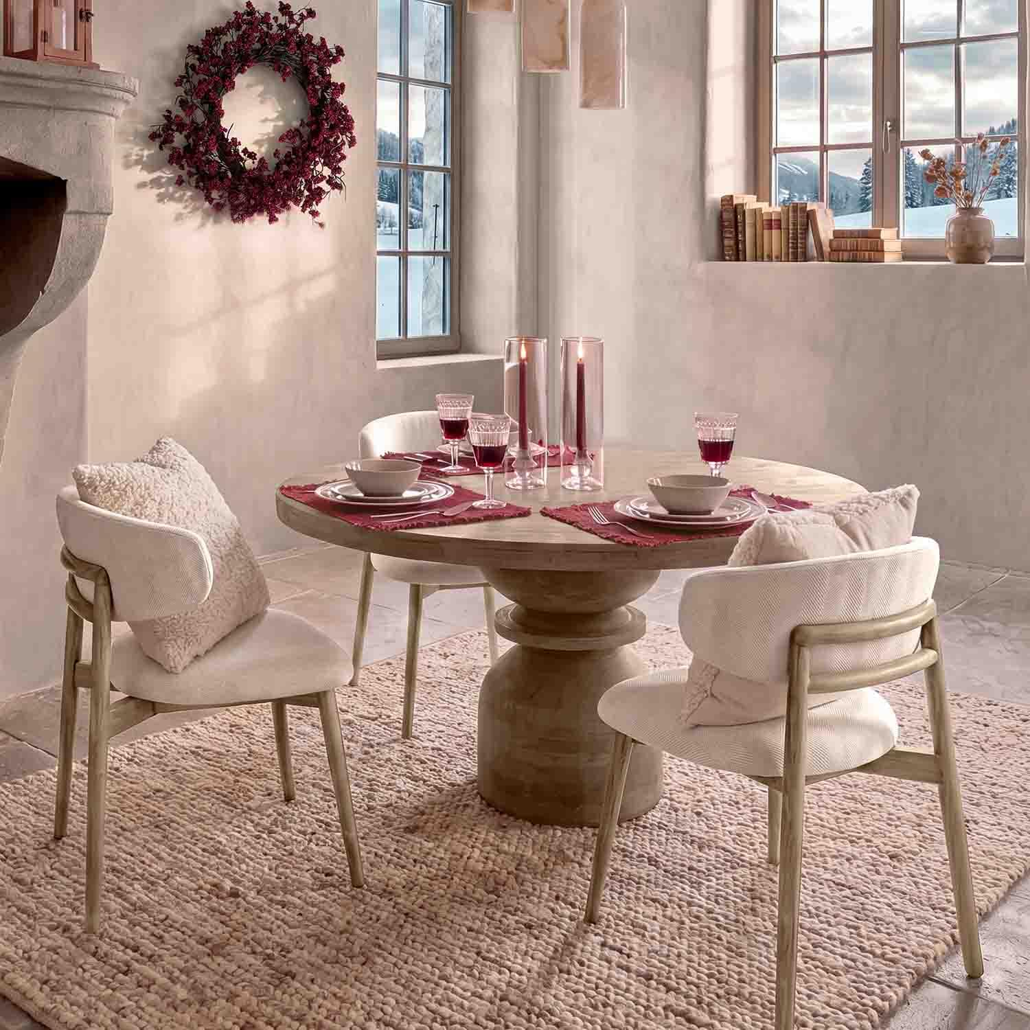 Chaises claires avec coussins autour d'une table ronde en bois décorée de bougies rouges et verres de vin